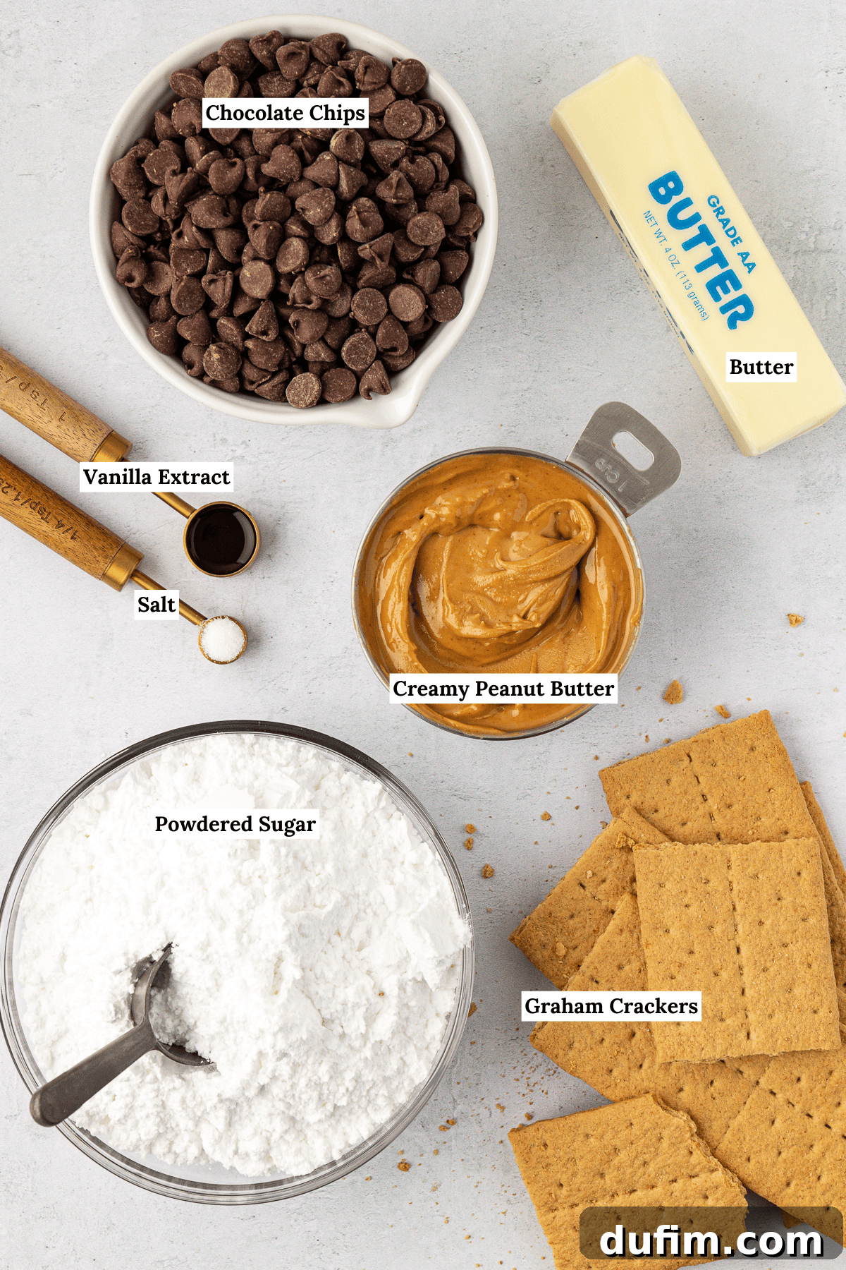 Overhead view of the ingredients for peanut butter bars including chocolate chips, a stick of butter, creamy peanut butter, vanilla extract, salt, powdered sugar, and graham crackers, neatly arranged.