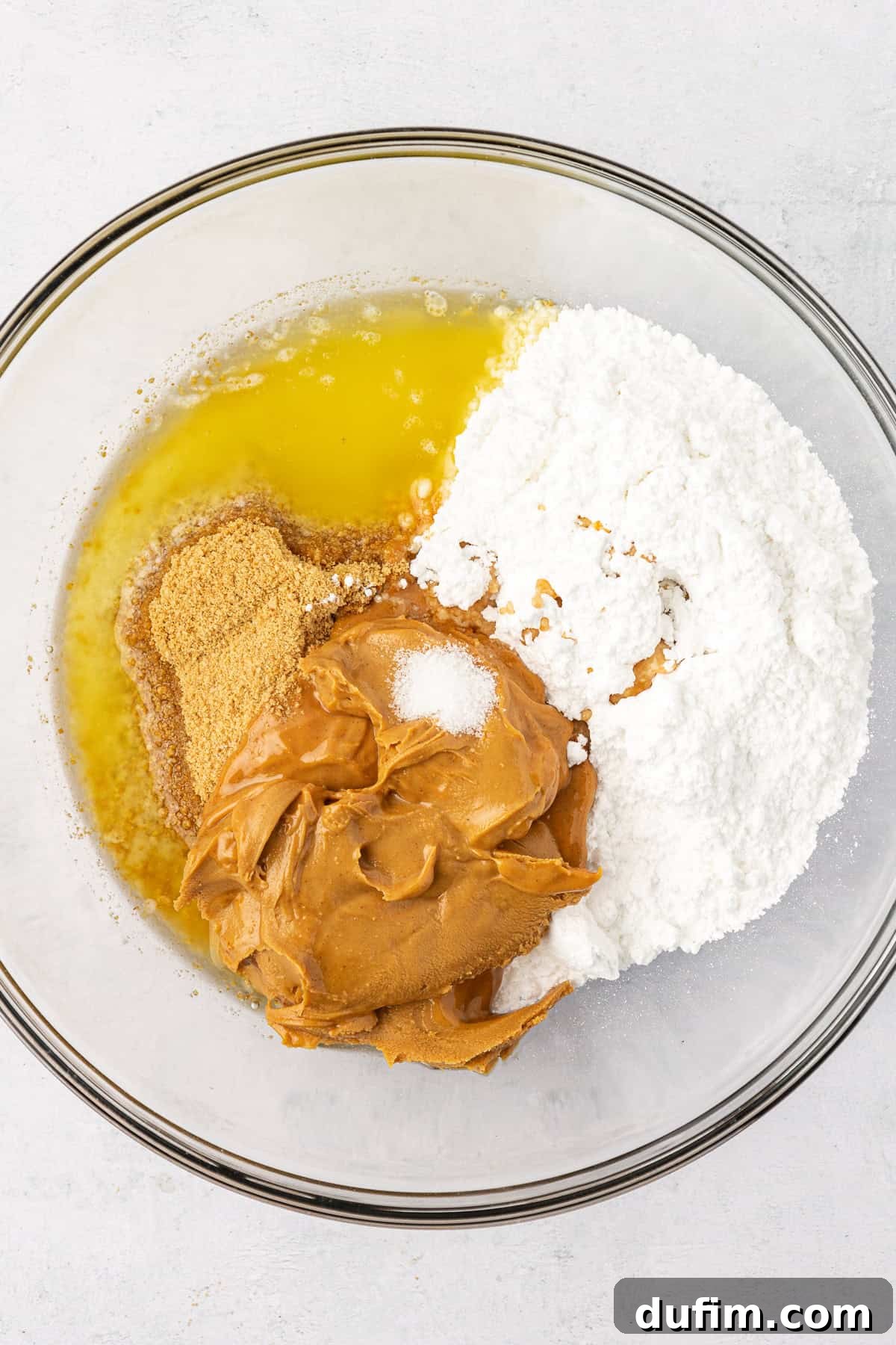 Melted butter, powdered sugar, graham cracker crumbs, and creamy peanut butter in a clear glass bowl, ready to be combined for the peanut butter base.