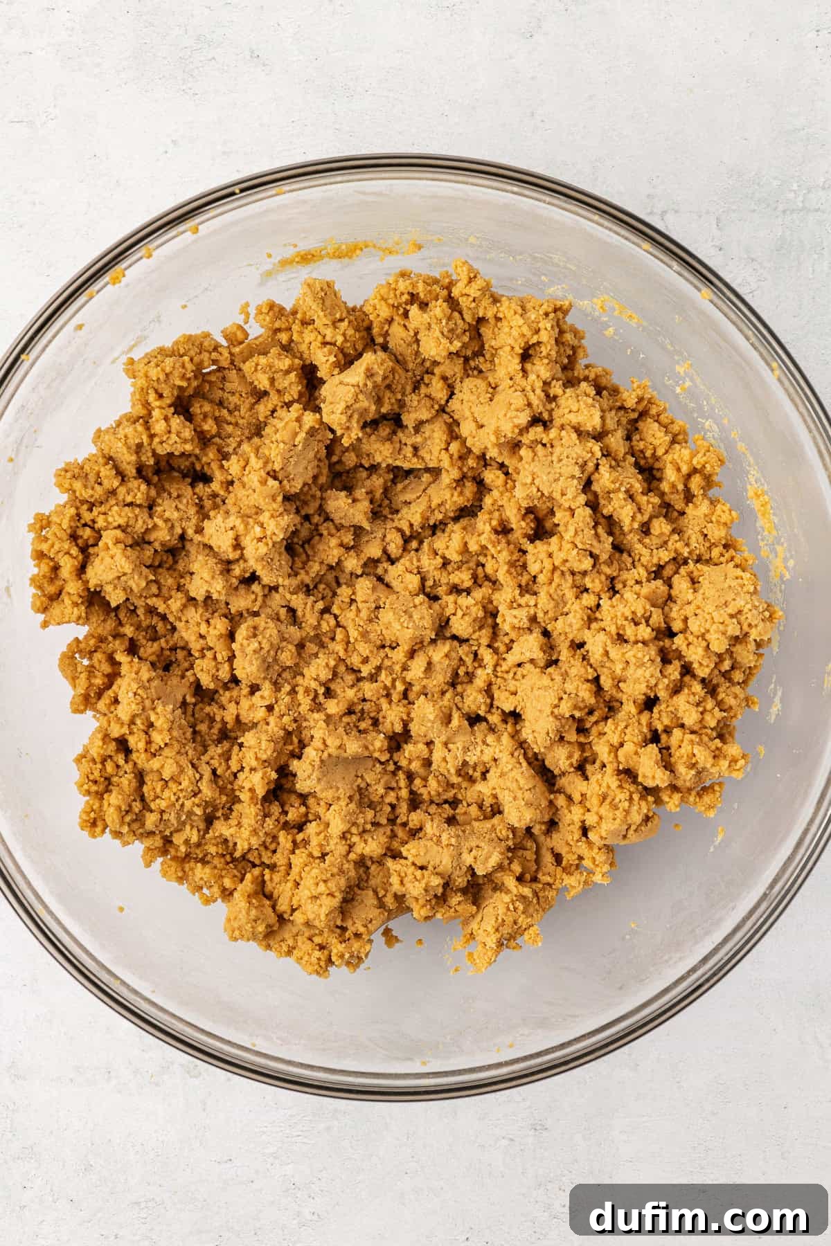 A peanut butter and graham cracker mixture for peanut butter bars in a clear glass bowl, showing its thick, uniform consistency after mixing.