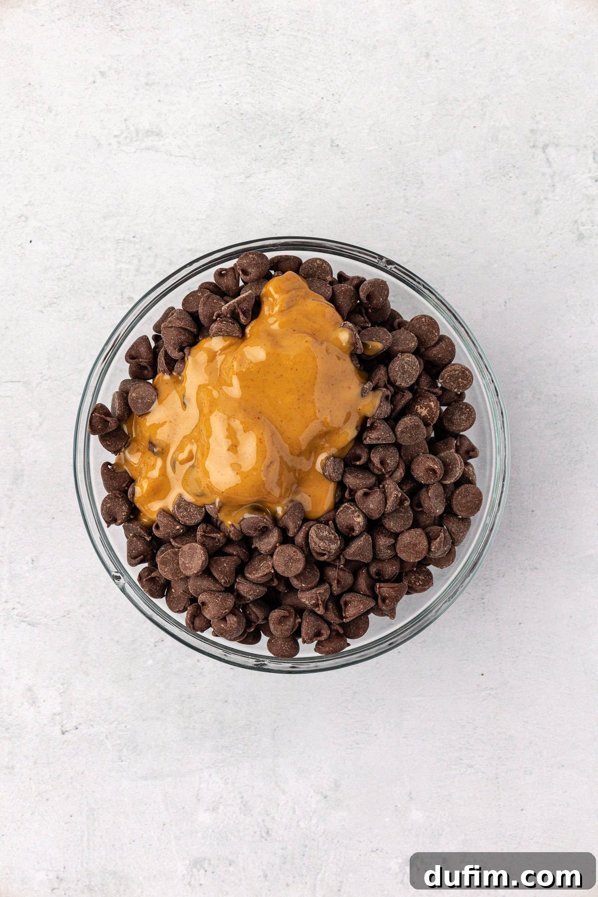 Chocolate chips and creamy peanut butter in a clear glass bowl, side-by-side, awaiting melting for the topping.