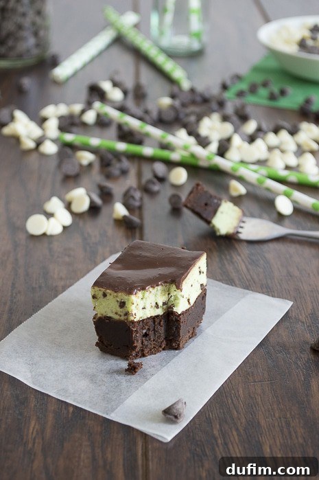 Rich, fudgy Mint Chip Mousse Brownies with three distinct layers: a dark brownie base, a vibrant green mint mousse, and a glossy chocolate glaze. The brownie is cut into squares, showing off its intricate structure and inviting texture.