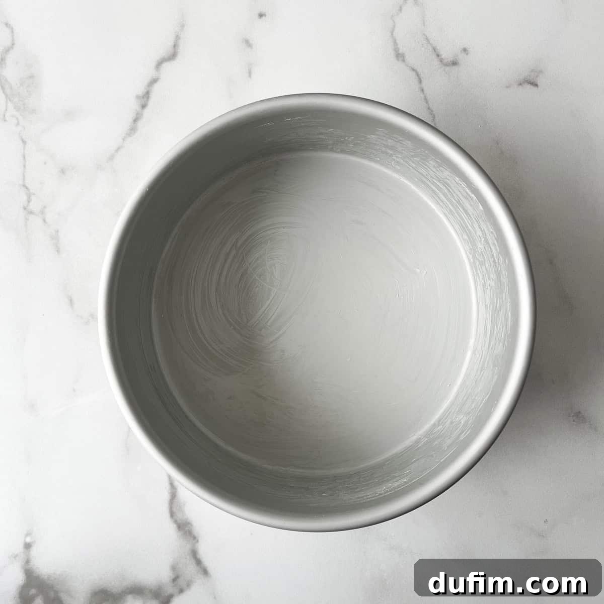 A round cake pan, perfectly greased with butter, resting on a clean countertop, ready for baking preparation.