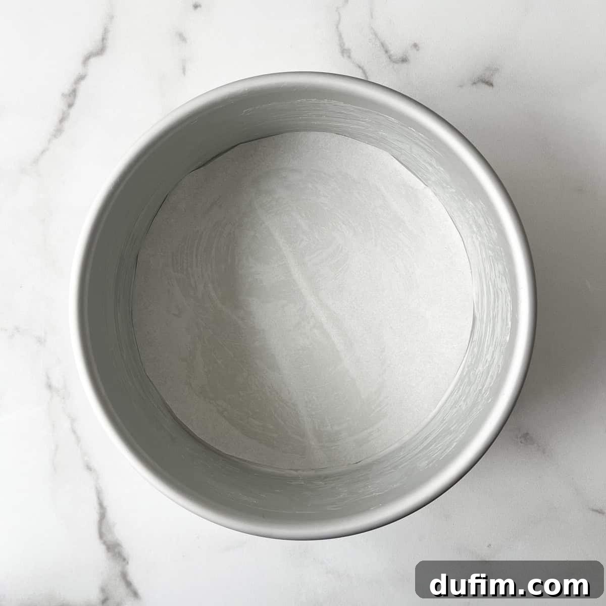 A round cake pan, expertly greased with butter and lined with a perfectly cut circle of parchment paper at the bottom, ensuring a smooth release for your gluten-free cake.