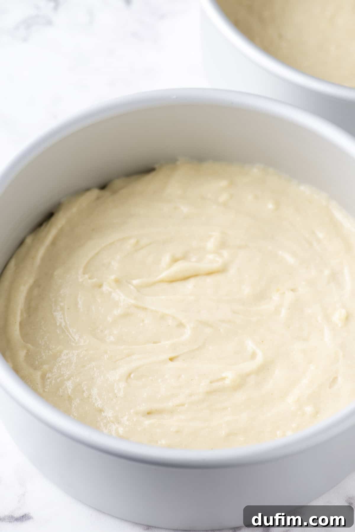 Smooth, golden-yellow cake batter perfectly leveled in a round cake pan, ready for baking.