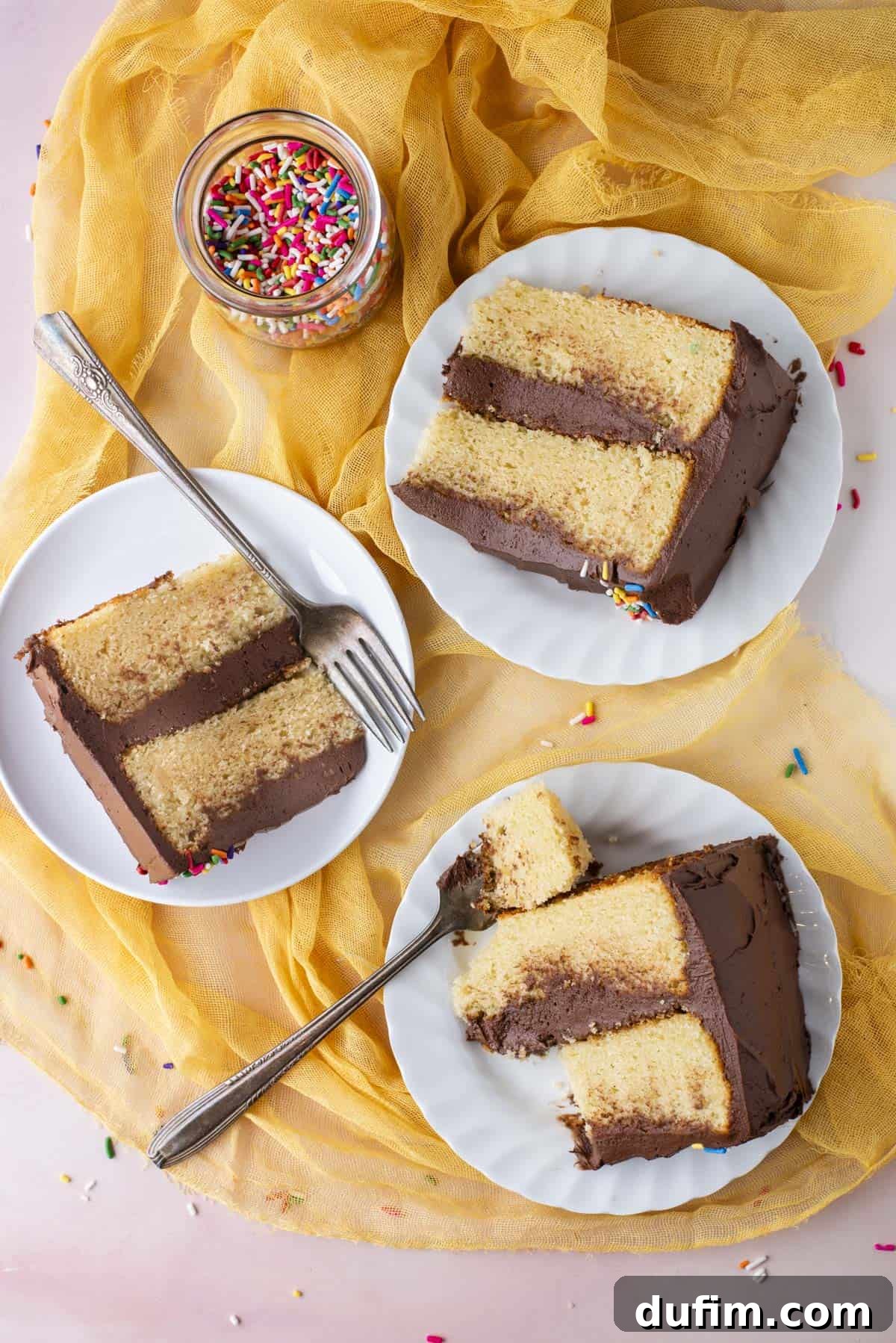An inviting overhead shot showcasing three pristine white plates, each holding a generous slice of gluten-free cake. The plates are arranged gracefully on a soft yellow cloth, with a charming jar of rainbow sprinkles and extra sprinkles scattered playfully around, creating a festive atmosphere.