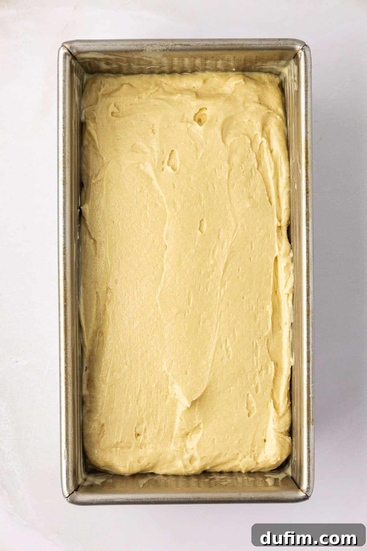 Rich, thick pound cake batter smoothly spread into a generously buttered loaf pan, perfectly prepared and ready for baking to achieve a classic homemade pound cake.