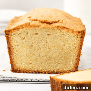 A perfectly baked classic pound cake with one slice gracefully cut off the end and laid beside it, revealing its moist, light yellow interior and inviting golden-brown outer crust. A picture of pure dessert perfection.