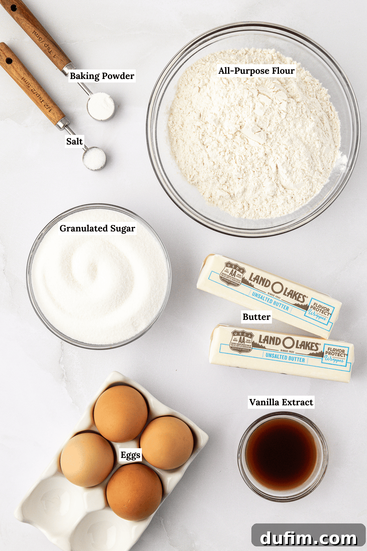 An inviting overhead shot showcasing all the essential ingredients for making the perfect homemade pound cake: baking powder, salt, all-purpose flour, two sticks of rich unsalted butter, granulated sugar, aromatic vanilla extract, and farm-fresh eggs, all ready for baking.