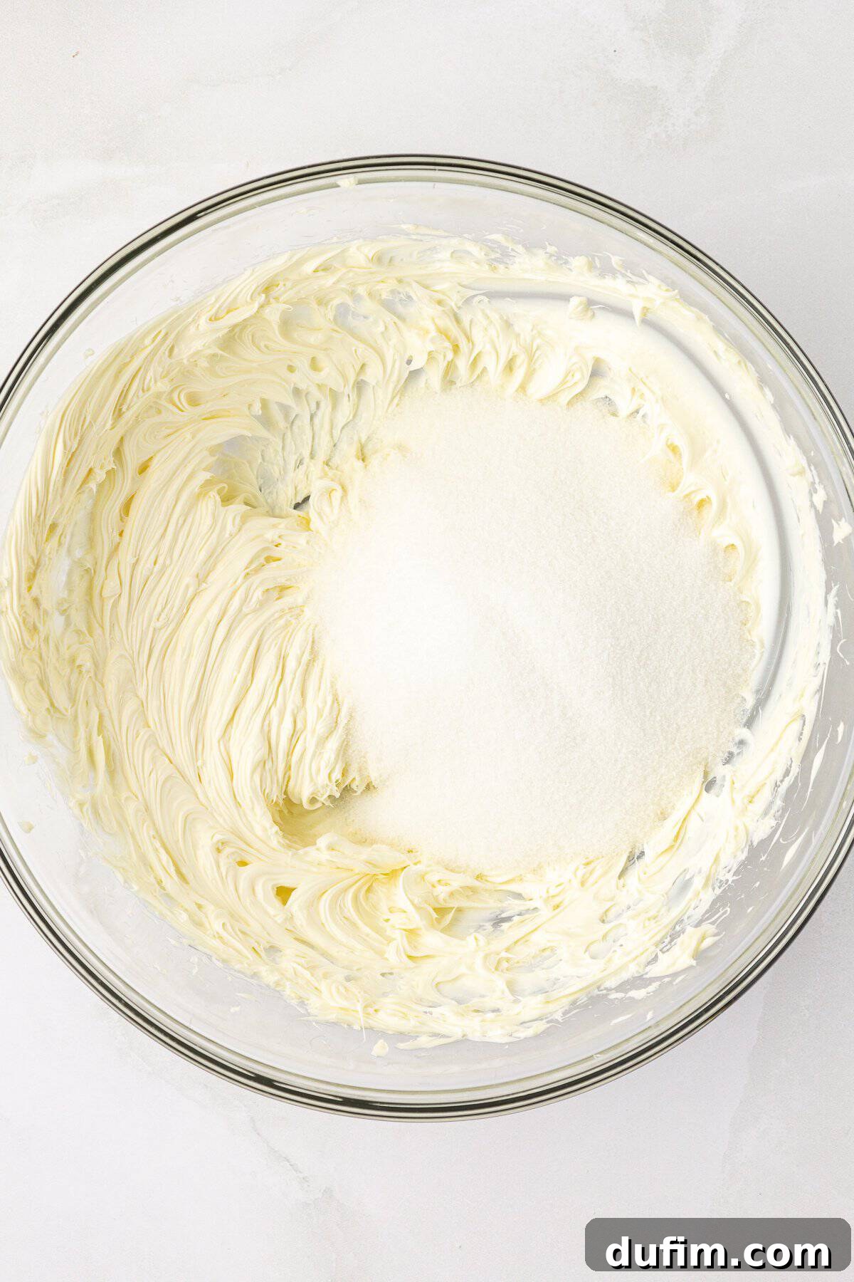 Room temperature butter freshly creamed in a clear glass mixing bowl, with granulated sugar sprinkled on top, ready to be beaten together for the pound cake batter.
