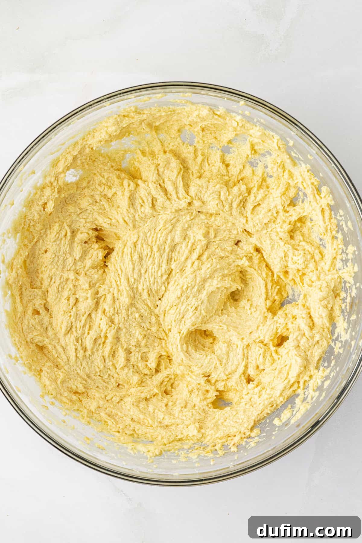 The fully mixed wet ingredients for a homemade pound cake, including butter, sugar, eggs, and vanilla, beautifully emulsified in a clear glass bowl, showcasing a smooth and consistent batter.