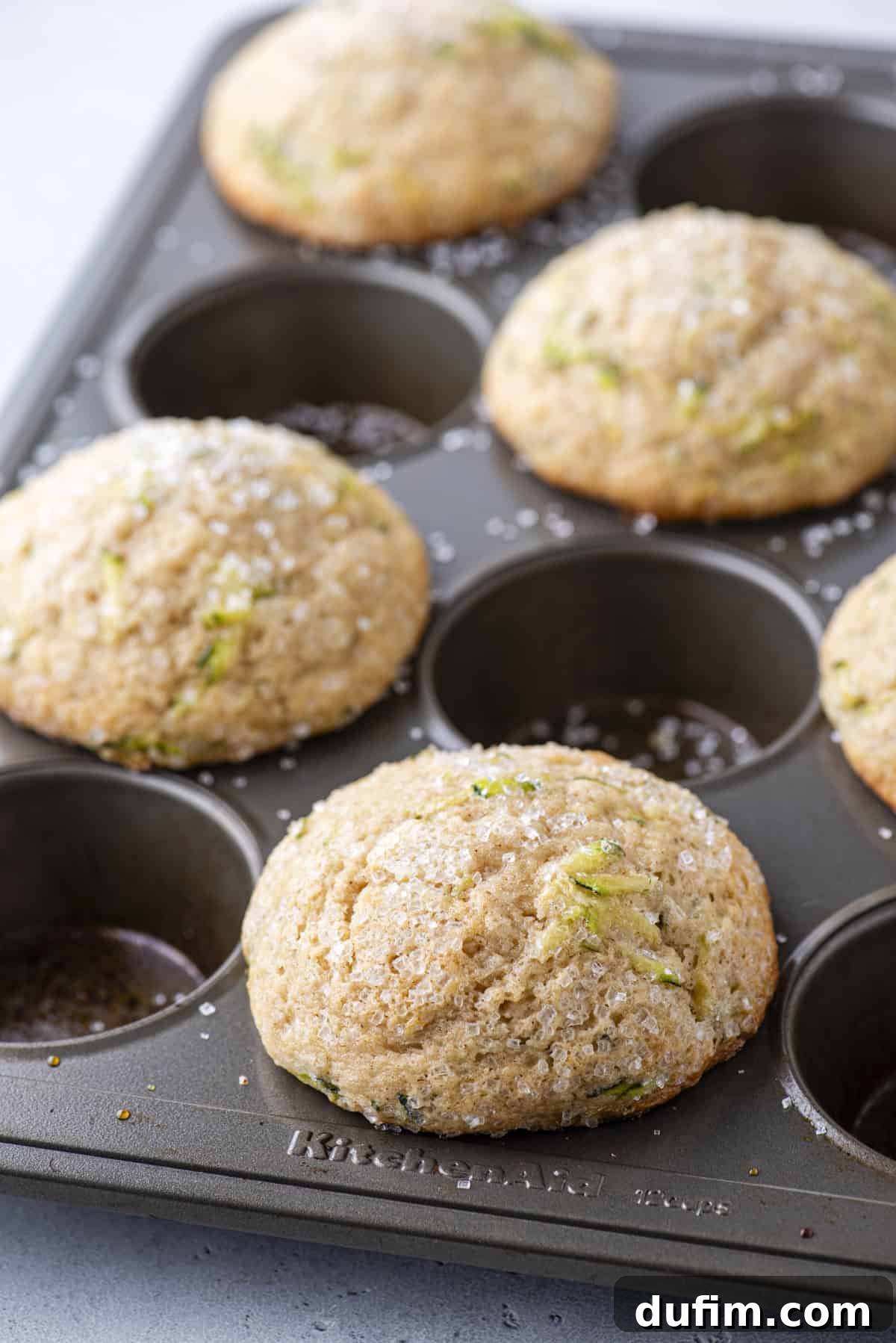 Freshly baked zucchini muffins rising beautifully in a muffin pan, with every other well filled, demonstrating the effectiveness of proper spacing for bakery-style results.