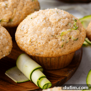 A beautifully baked zucchini muffin sits on a wooden plate, accompanied by a decorative spiral of zucchini peel, inviting you to taste its homemade goodness.