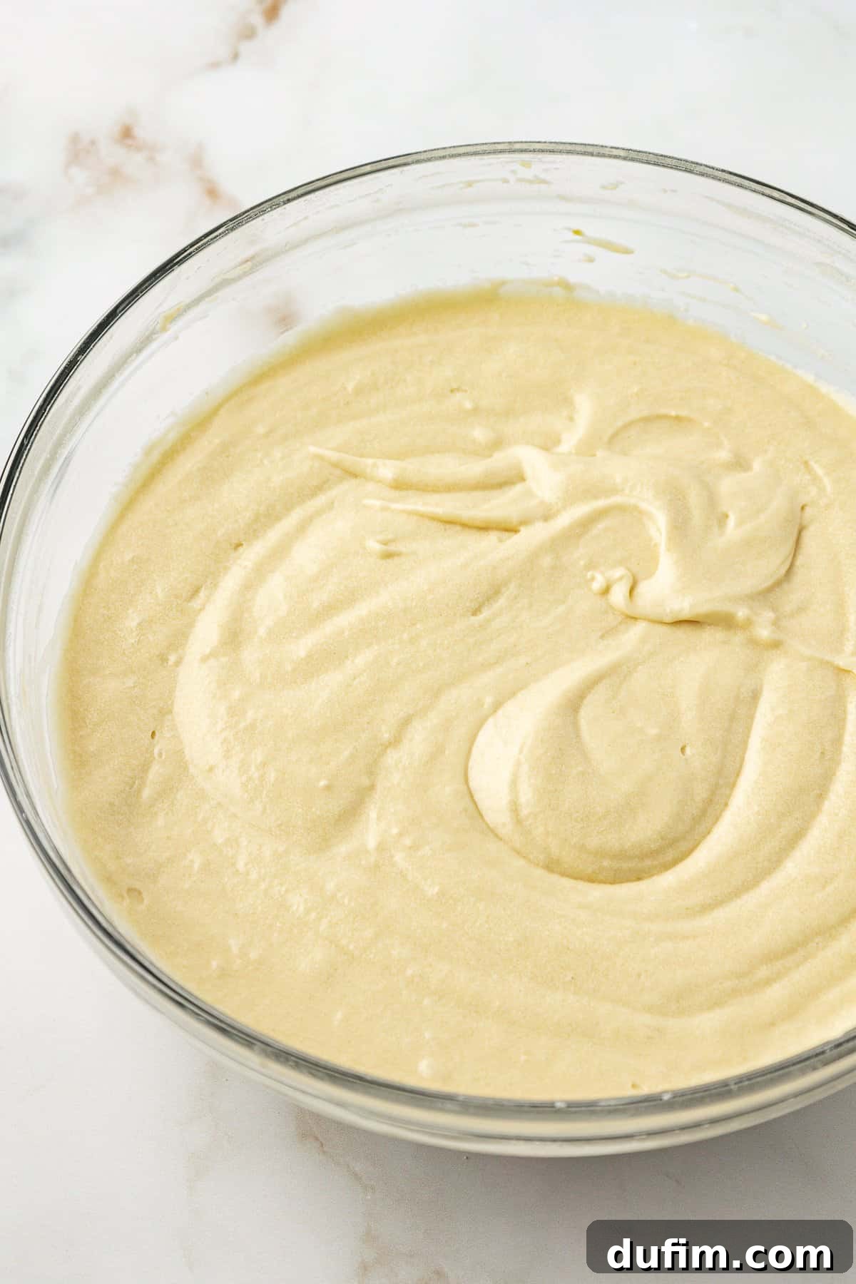 Smooth, consistent vanilla cake batter in a clear glass bowl, after the wet and dry ingredients have been gently combined.