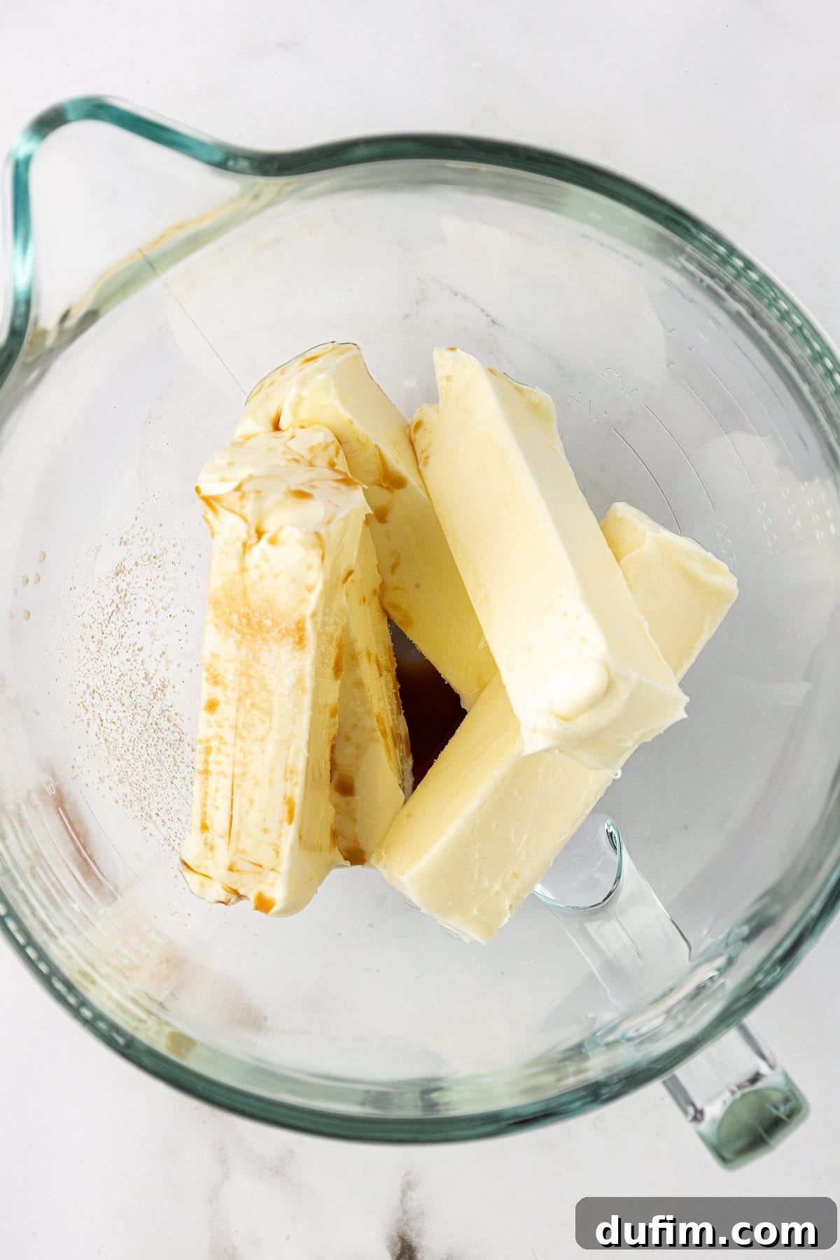Softened butter, vanilla extract, and salt combined in a clear glass mixing bowl, ready to be beaten for frosting.