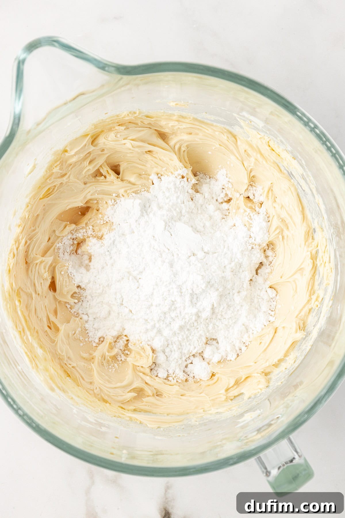 Vanilla frosting ingredients mixed together with a generous pile of powdered sugar on top, ready to be fully incorporated.