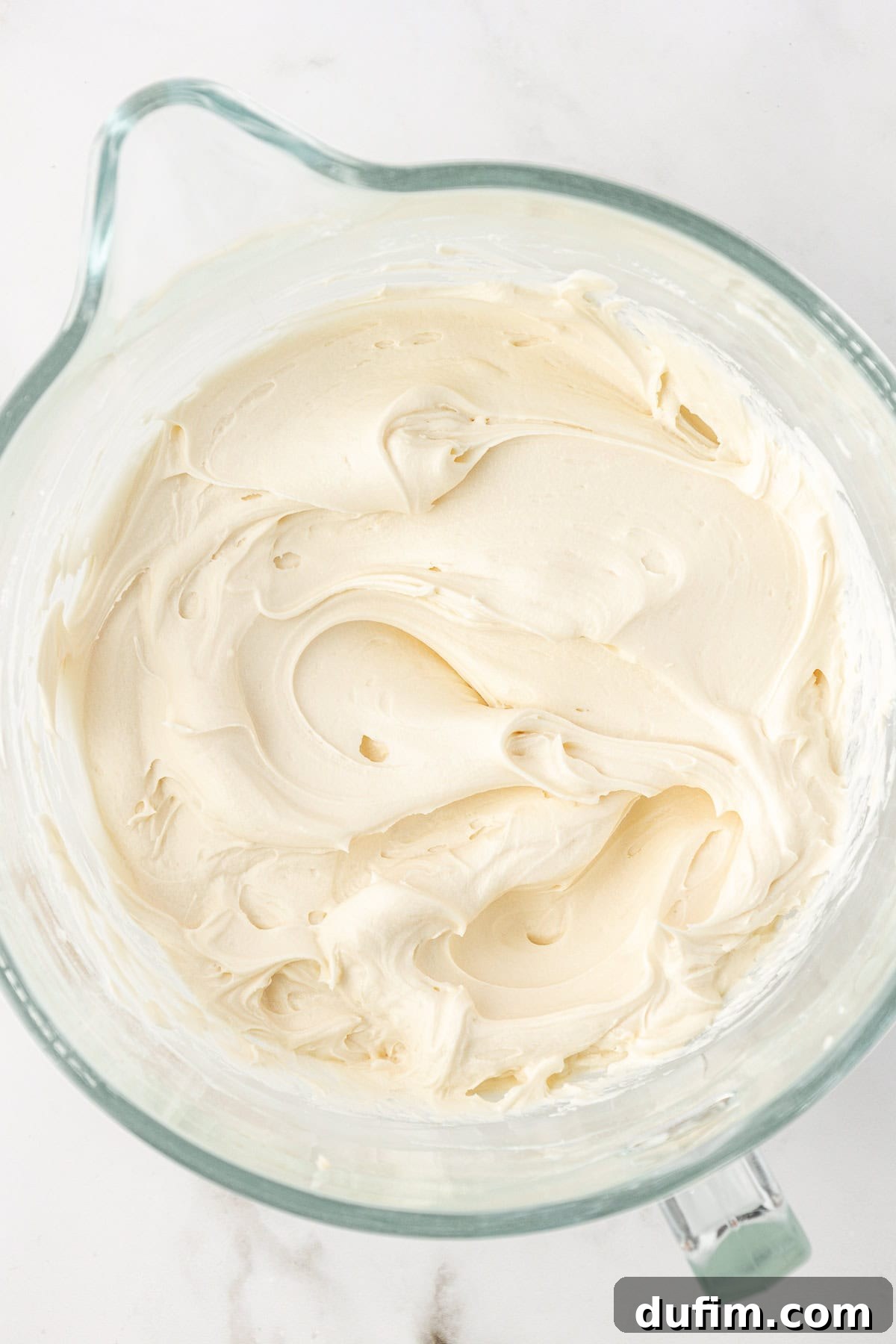 Smooth and creamy vanilla frosting in a clear glass bowl, ready for spreading on the cake.