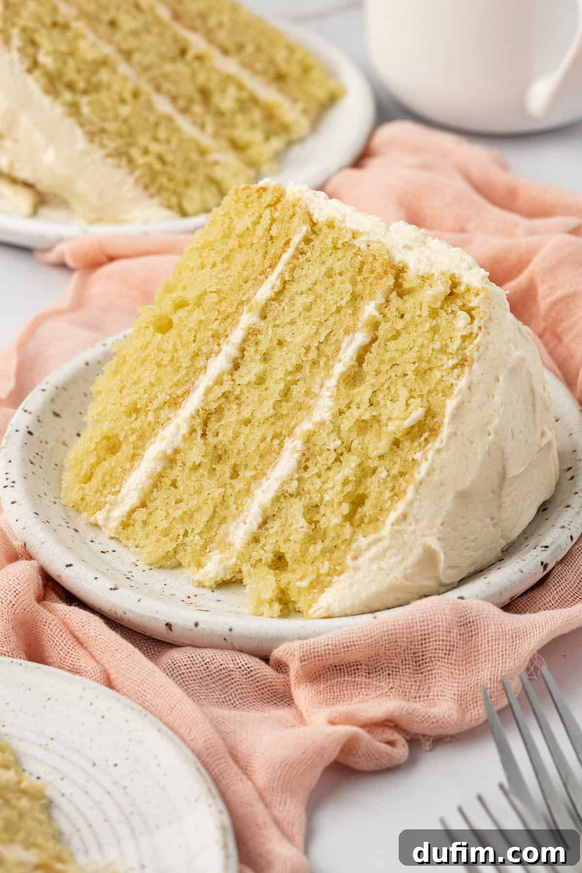 Multiple slices of vanilla cake arranged on white plates on a pink cloth, accompanied by forks and a white cup, ready to be enjoyed.