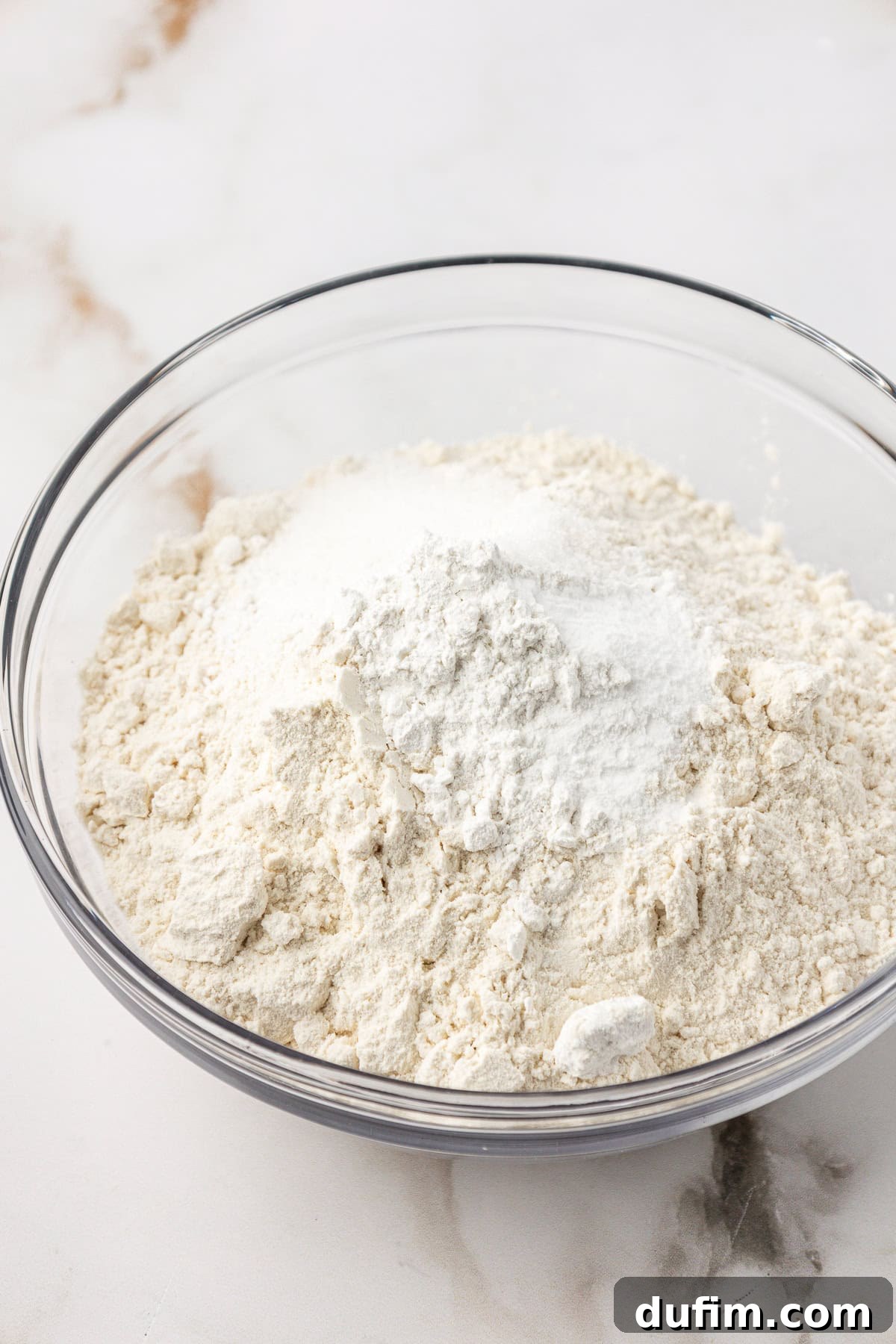 Dry ingredients for the cake, including flour, baking powder, baking soda, and salt, resting in a clear glass mixing bowl.