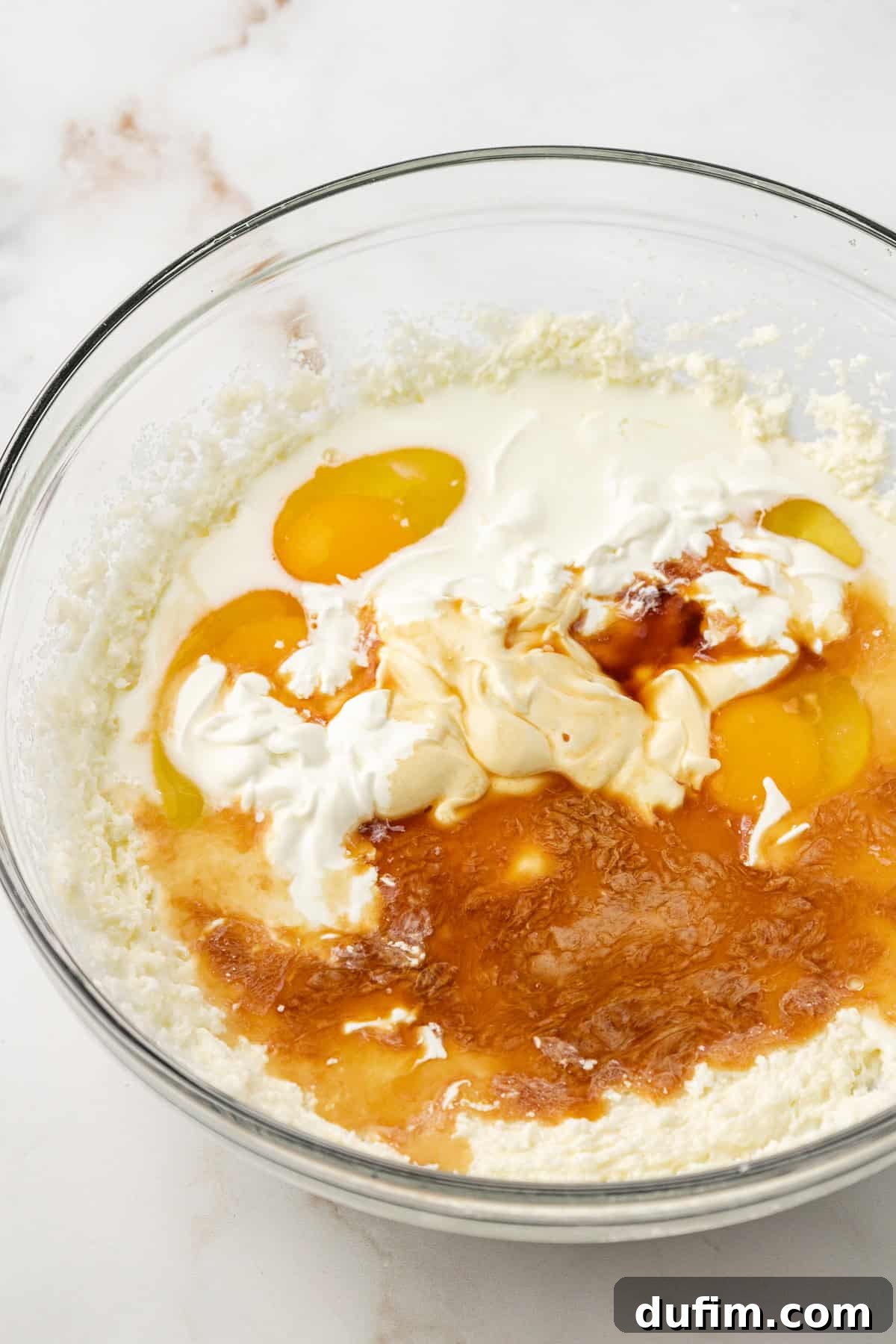 Eggs, sour cream, milk, and vanilla extract carefully added on top of the creamed butter and sugar mixture in a clear glass bowl.
