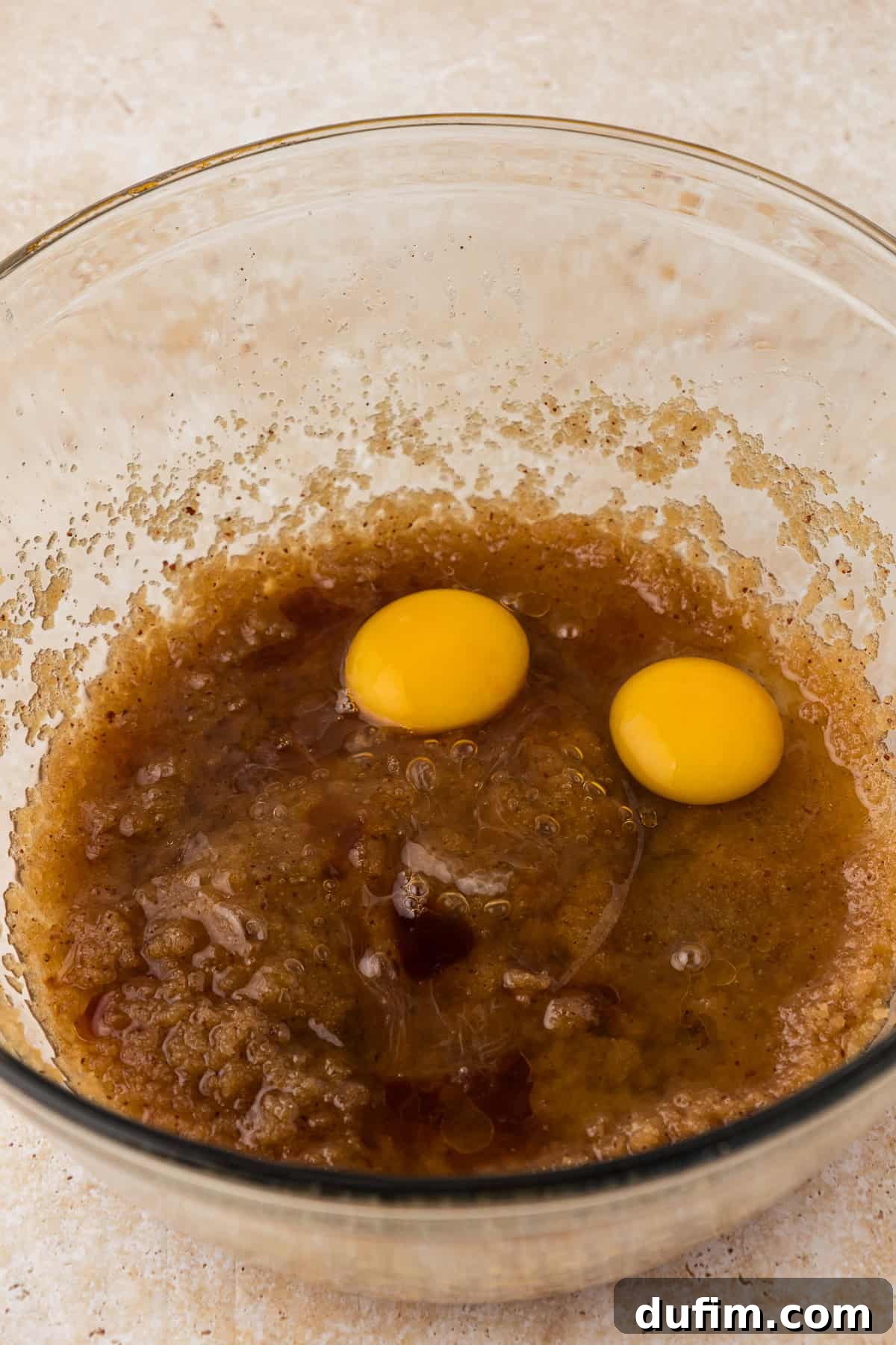 The rich wet ingredients for pizookie in a clear glass bowl, now topped with two fresh eggs, ready to be incorporated for added moisture and binding.