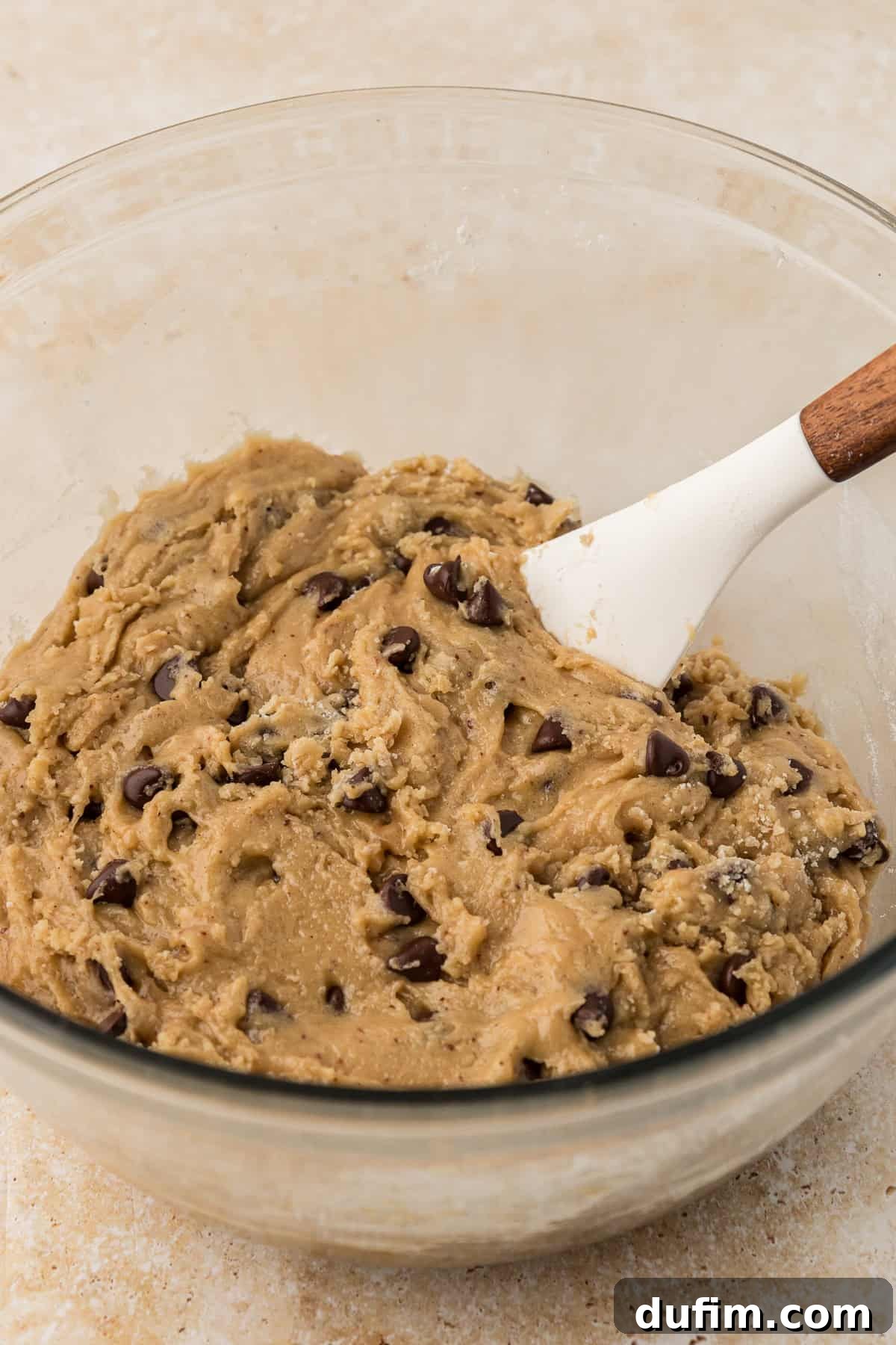 A glass bowl containing the rich, thick pizookie batter, with a spatula resting in it, showcasing the perfect consistency before baking.