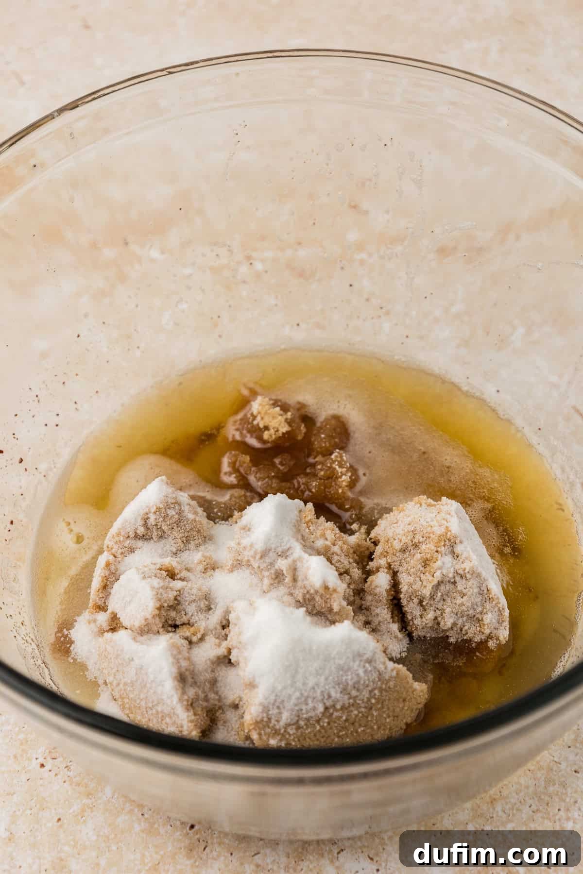 A clear glass bowl holding the luscious combination of brown sugar, granulated sugar, and other wet ingredients, ready for mixing to create the pizookie's rich base.