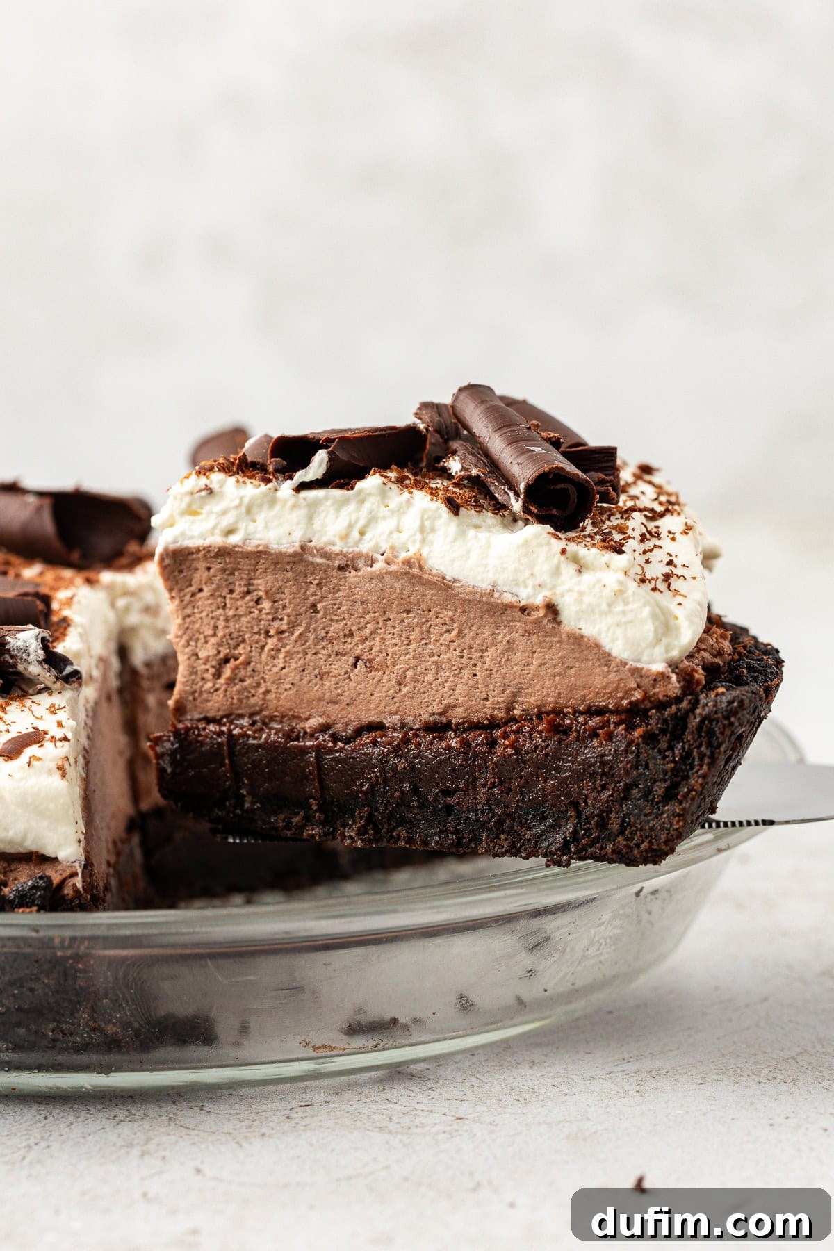 side view of a slice of mud pie being lifted out of a glass pie dish away from the rest of the pie