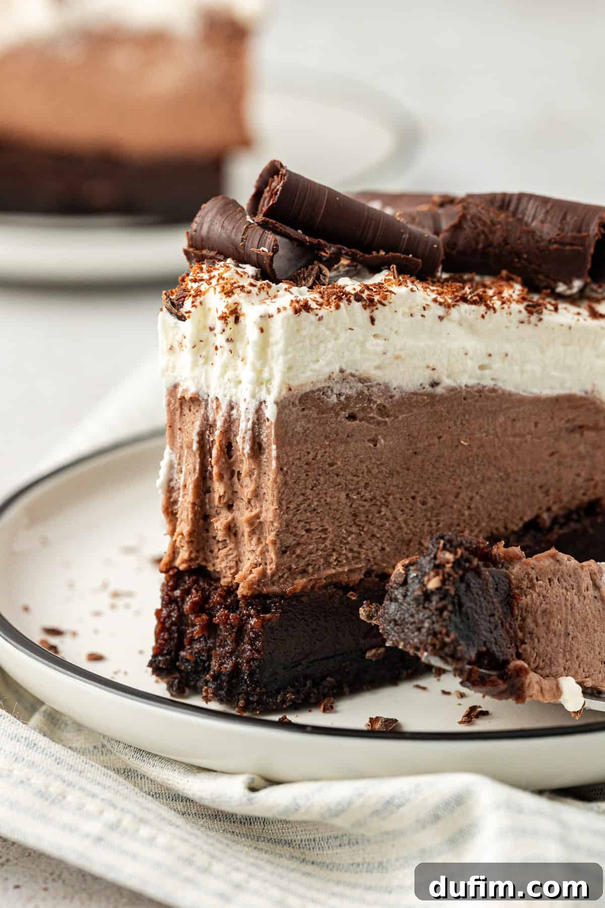 side view of a slice of mud pie on a white plate with a fork that has one bite out of the pie on it, leaning on the plate