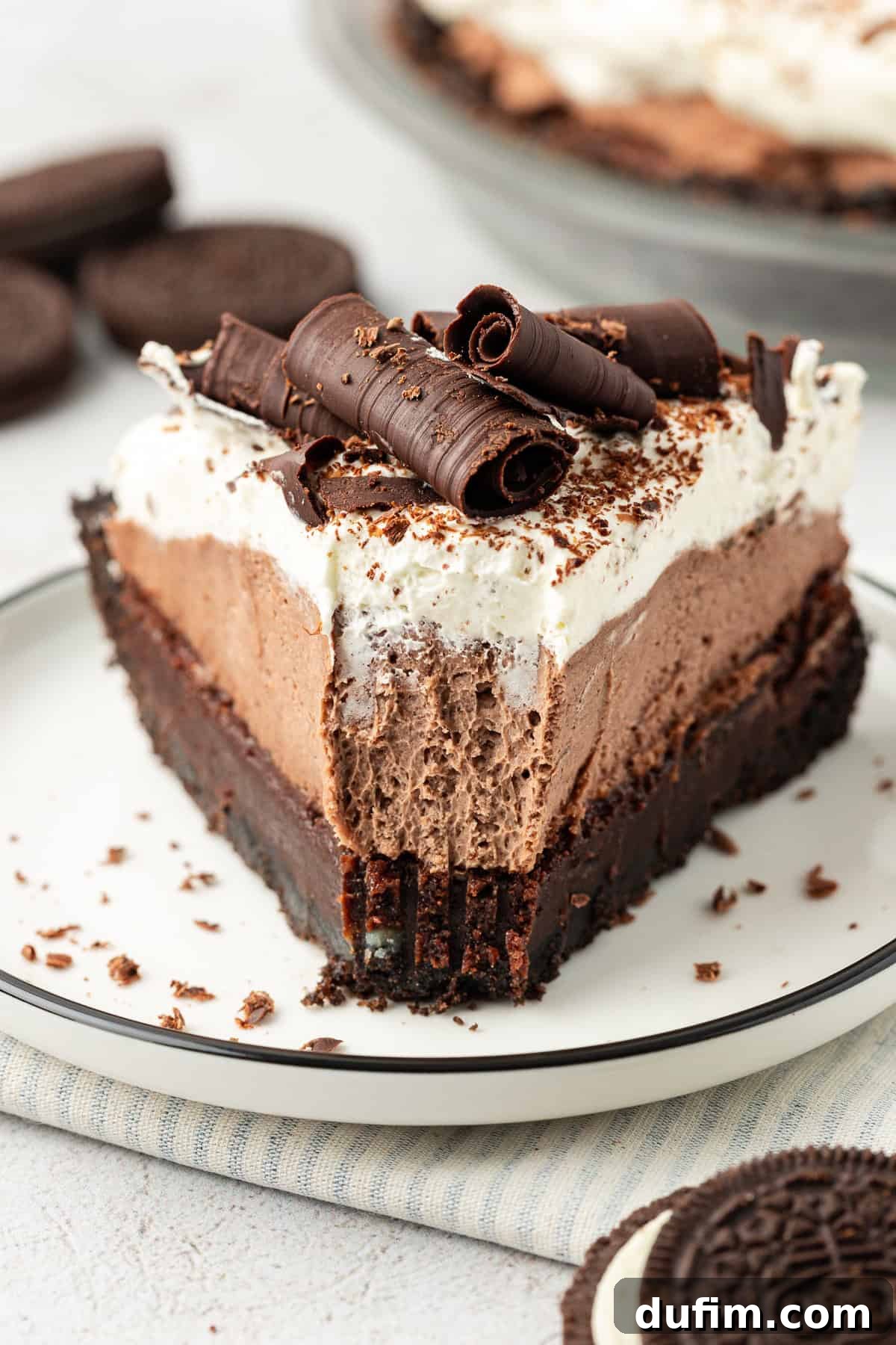 a slice of mud pie on a small white plate with a bite missing out of the tip of the pie and whole oreos scattered around
