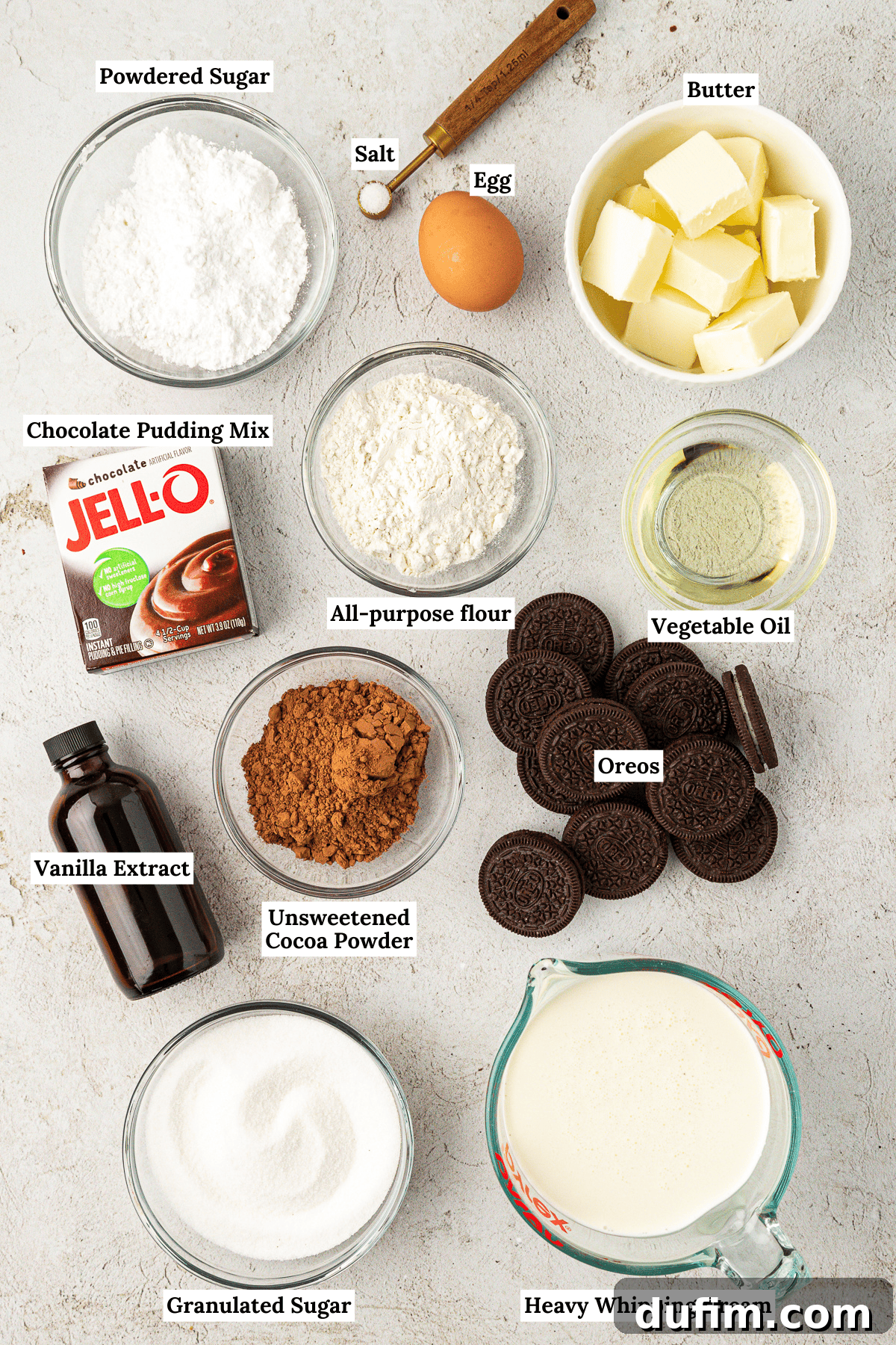 over head view of ingredients for mud pie including powdered sugar, salt, egg, butter, chocolate pudding mix, all-purpose flour, vegetable oil, vanilla extract, unsweetended cocoa powder, oreos, granulated sugar, and heavy whipping cream