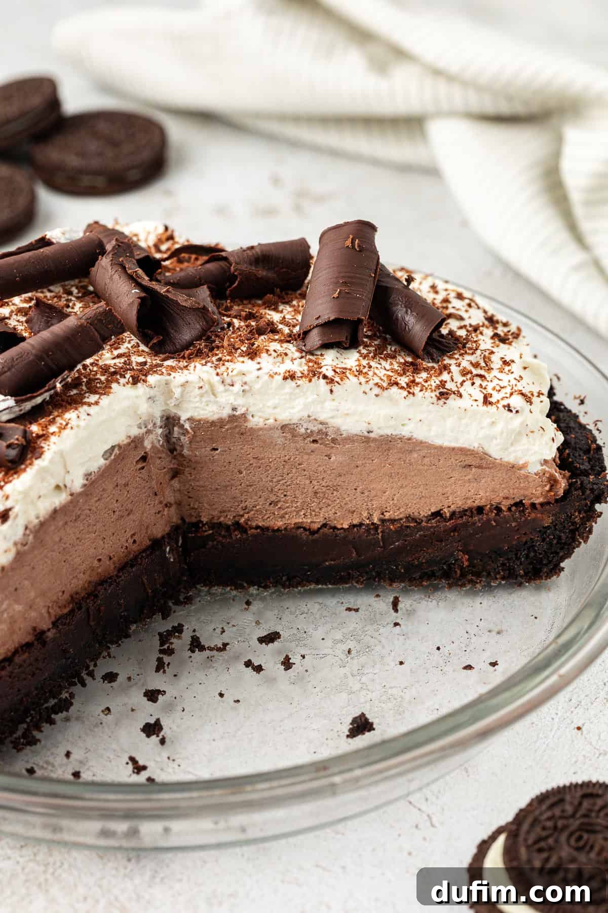 mud pie in a clear glass pie dish with slices missing, exposing the inside of the pie layers, with oreos and a white kitchen towel scattered around