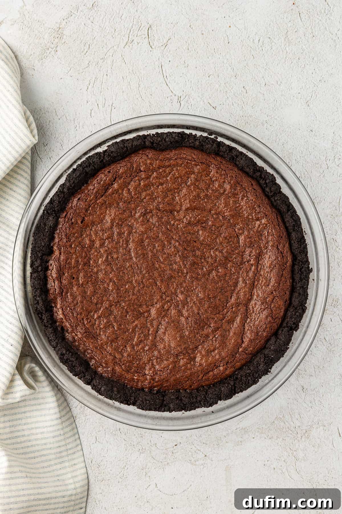 a clear glass pie dish with oreo crust and a brownie layer baked in it