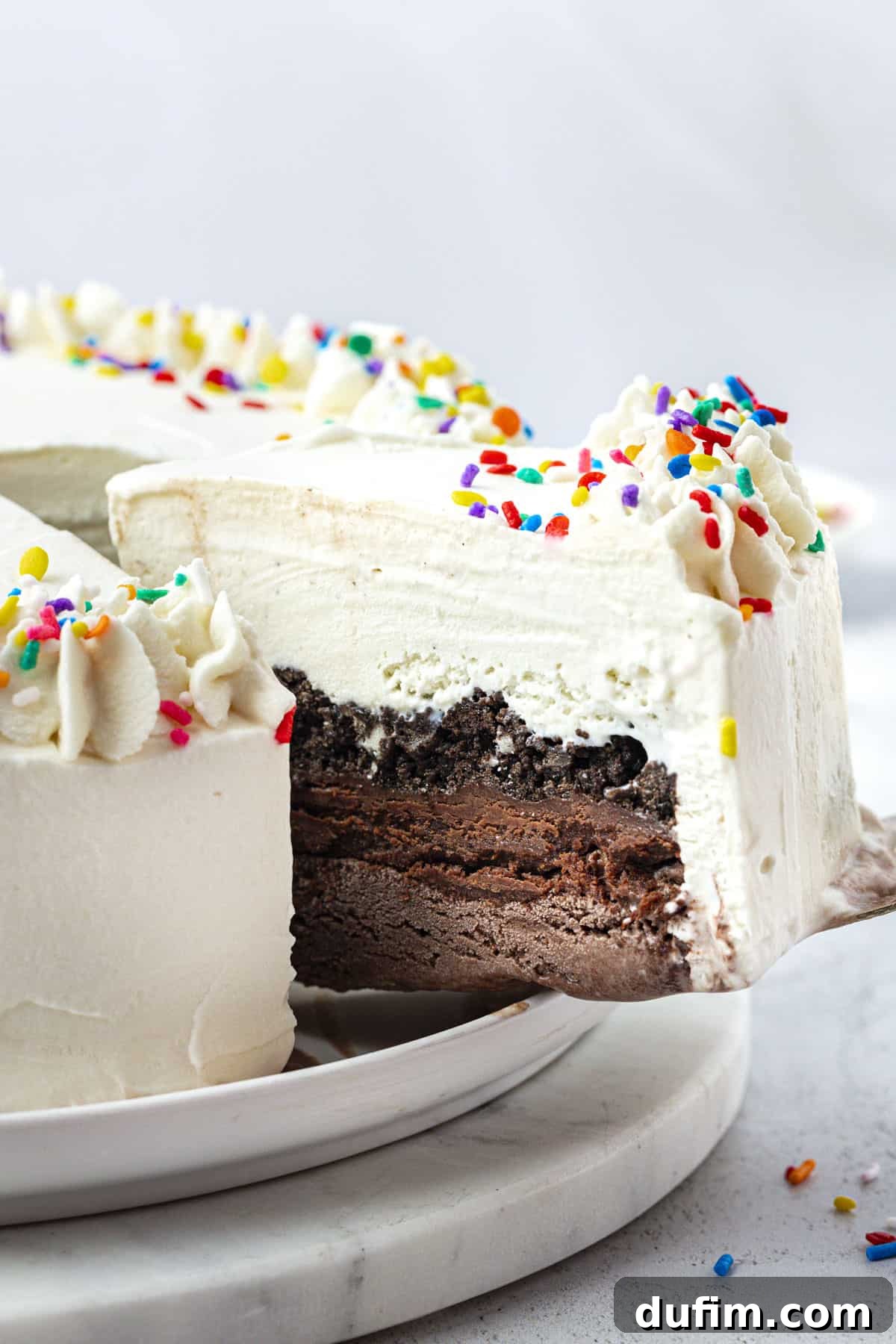 A perfect slice of layered ice cream cake being carefully lifted away from the main cake with a spatula, highlighting the distinct layers.