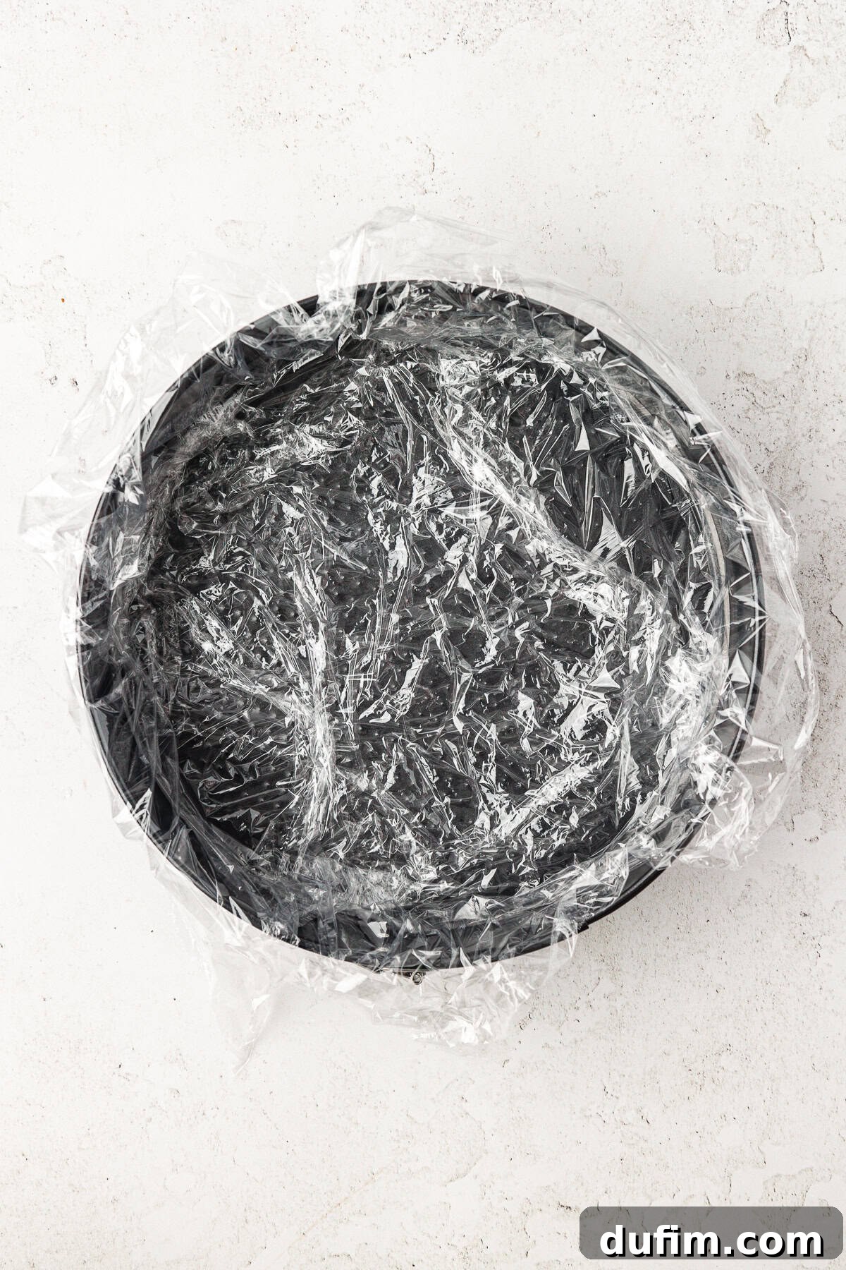 A springform pan meticulously lined with plastic wrap, ready for the first layer of ice cream cake.