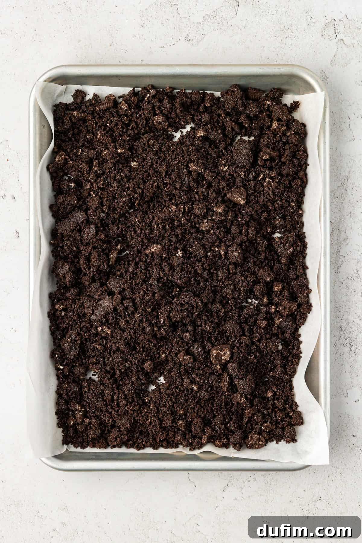 Finely crushed Oreo cookies ready for the chocolate crunch layer, spread on a baking sheet lined with parchment paper.