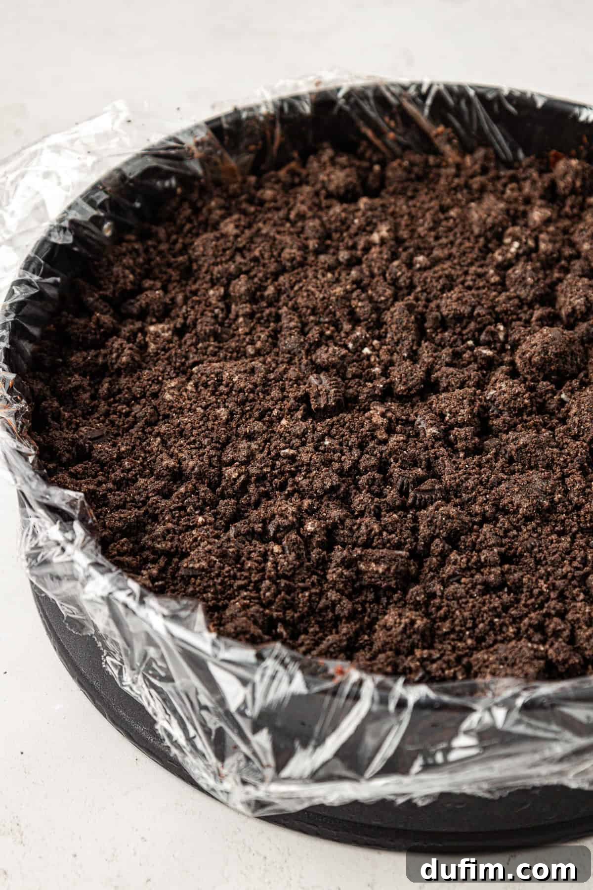The crispy chocolate crunch layer made from crushed Oreos, evenly distributed over the ganache in a plastic-lined springform pan.