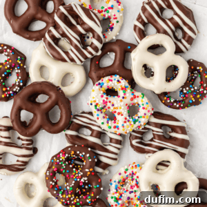 An assortment of chocolate covered pretzels stacked and scattered around, including dark chocolate with white chocolate drizzle, white chocolate with dark chocolate drizzle, and both dark and white chocolate coated in colorful rainbow sprinkles.