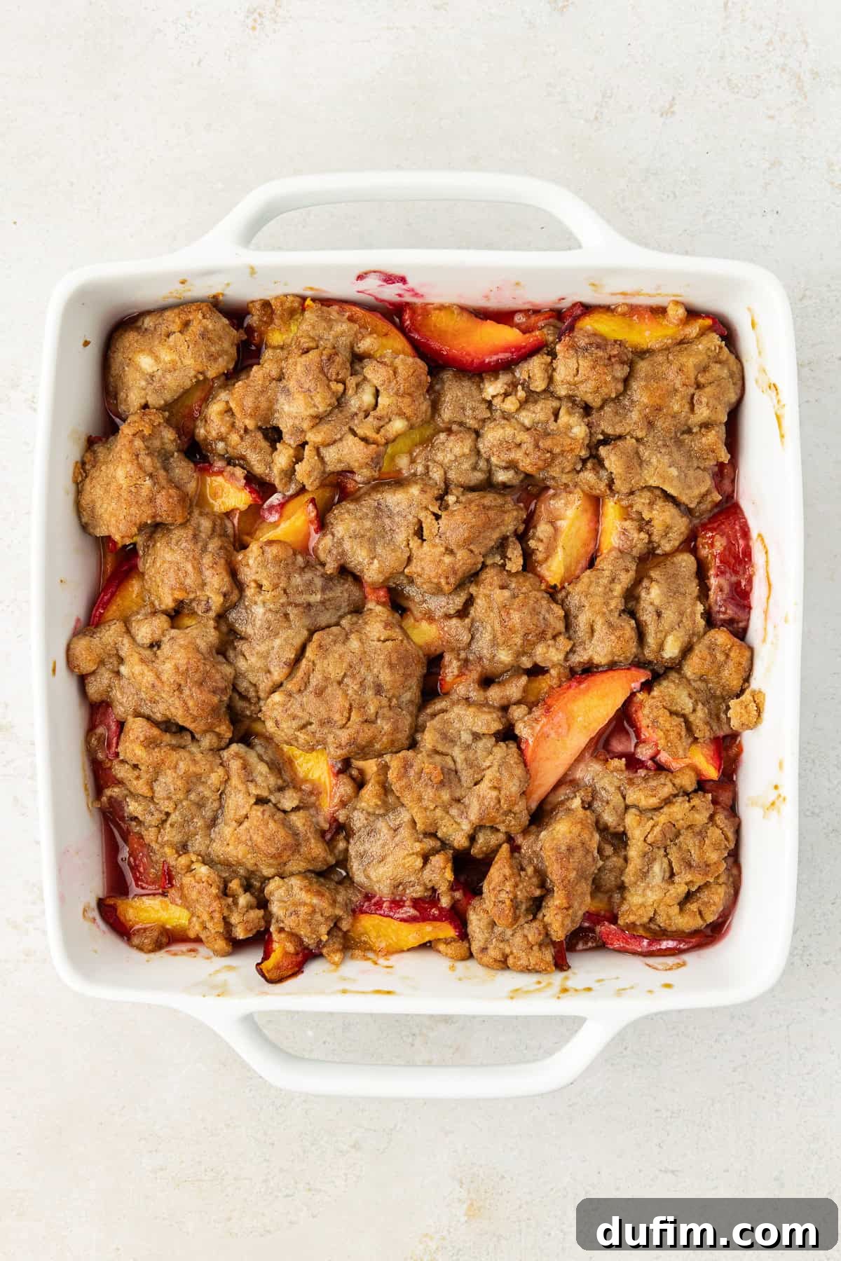 Irresistible Homemade Peach Cobbler 9 Overhead view of freshly baked peach cobbler in a square white baking dish, with a golden-brown, bubbly topping.