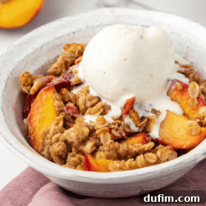 A small white bowl with a serving of peach crisp, topped with a scoop of vanilla ice cream, ready to be enjoyed.