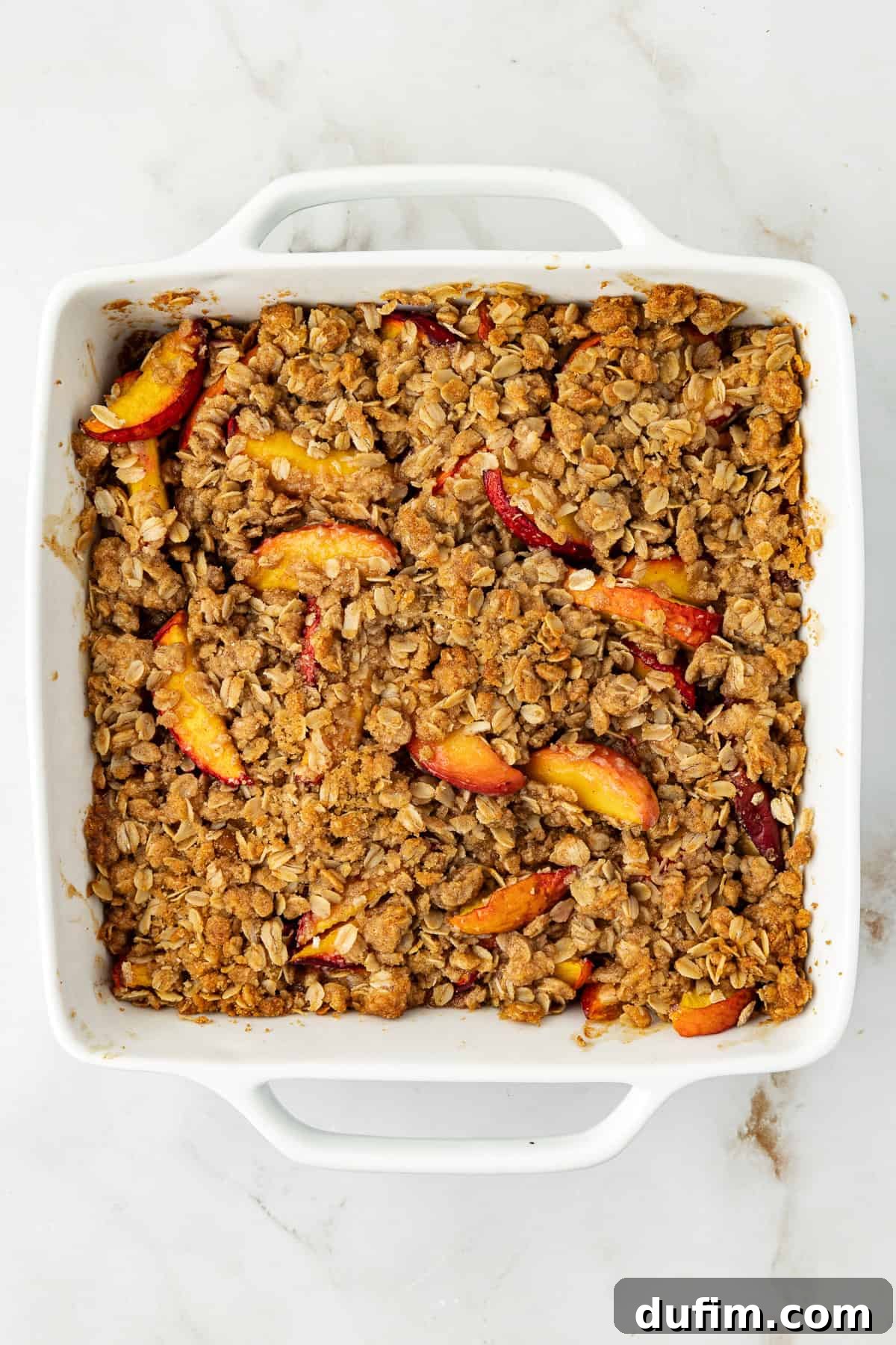 Overhead view of a perfectly baked peach crisp in a square white baking dish, golden-brown and bubbling, fresh from the oven.