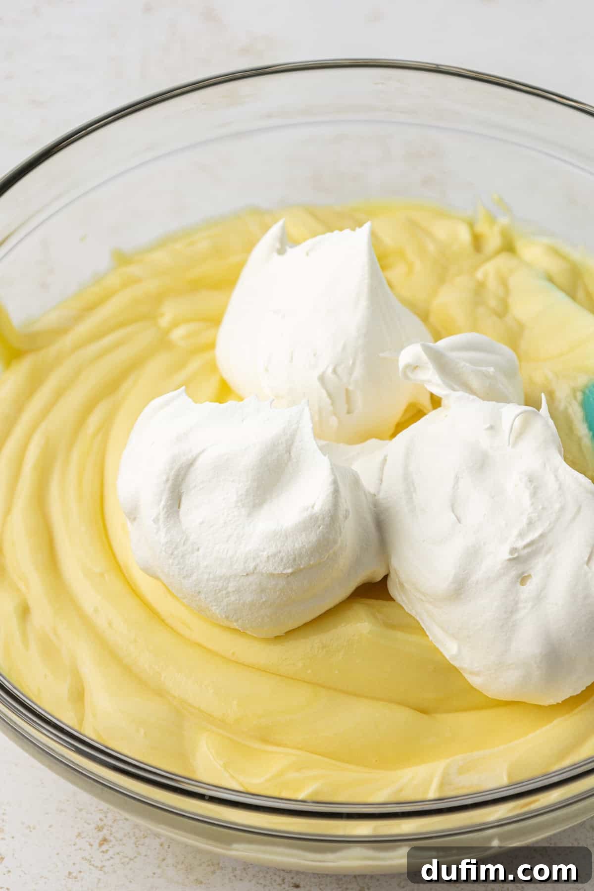 Mastering Delicious Dirt Cake 11 The smooth vanilla instant pudding mixture in a clear glass bowl, topped with a generous layer of fluffy whipped topping, awaiting gentle incorporation.