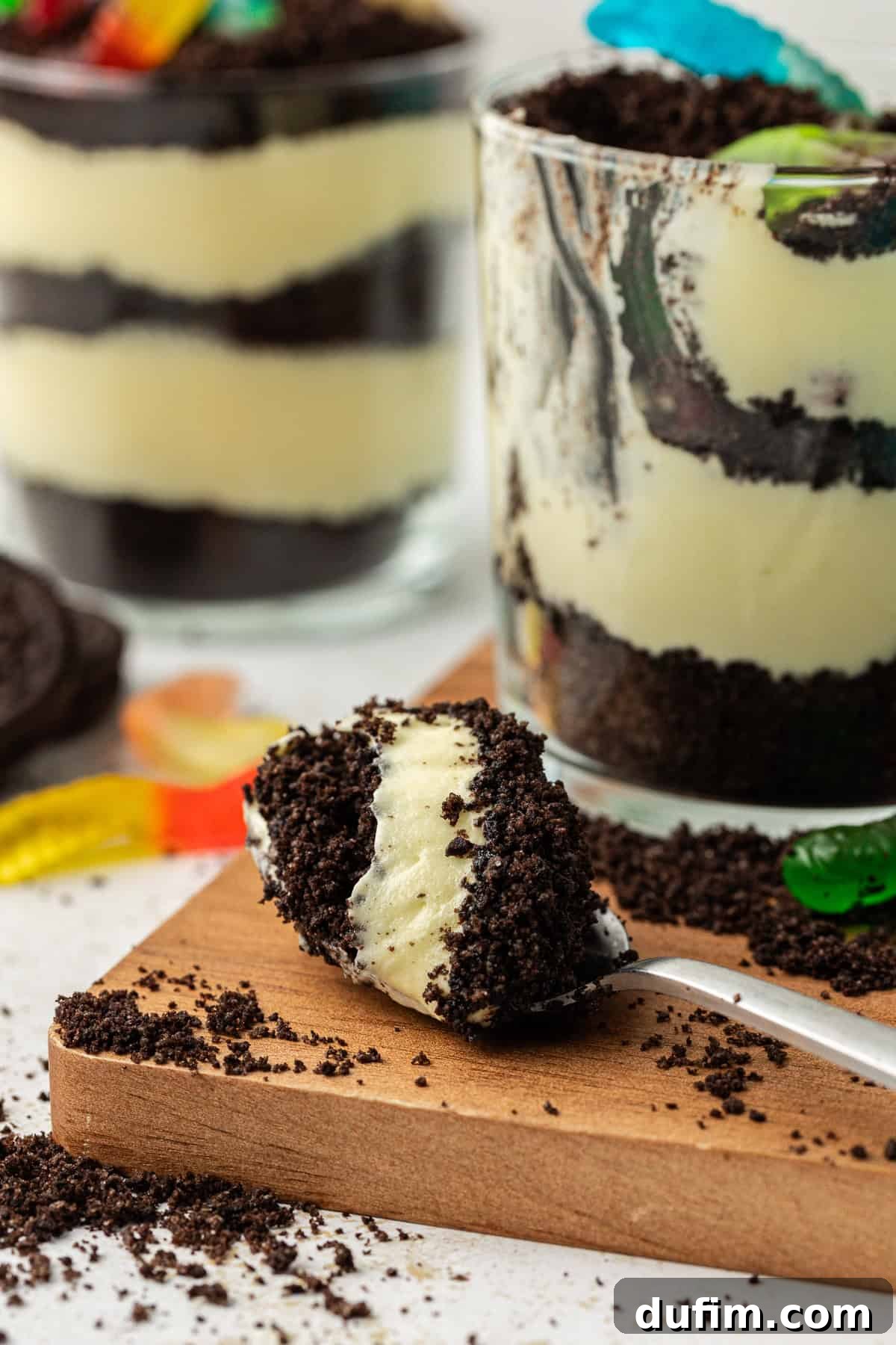Mastering Delicious Dirt Cake 13 A spoonful of irresistible dirt cake resting on a rustic wooden platter, artfully arranged beside several small individual trifle dishes of dirt cake, all adorned with extra Oreo crumbs and colorful gummy worms, highlighting the inviting texture and presentation.