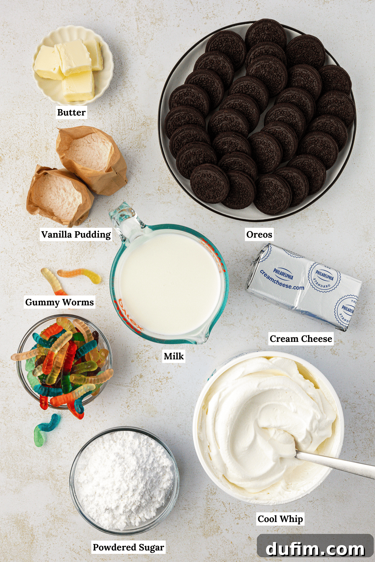 Mastering Delicious Dirt Cake 4 An overhead view showcasing all the essential ingredients for making dirt cake, including milk, instant vanilla pudding mix, Oreo cookies, softened unsalted butter, cream cheese, powdered sugar, and a bag of colorful gummy worms.