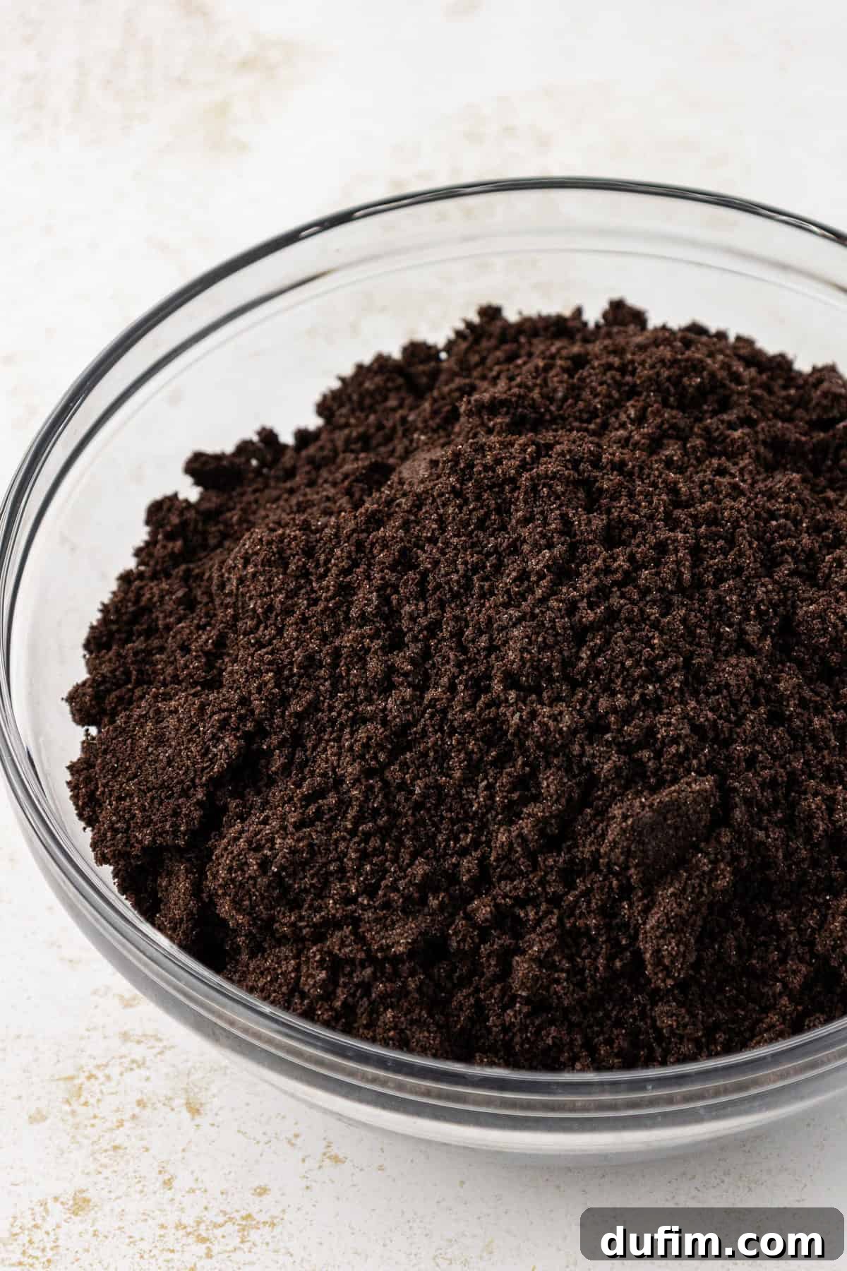 Mastering Delicious Dirt Cake 5 Finely crushed Oreo cookies ready for layering, presented in a clear glass bowl, showcasing the ideal 'dirt' texture.
