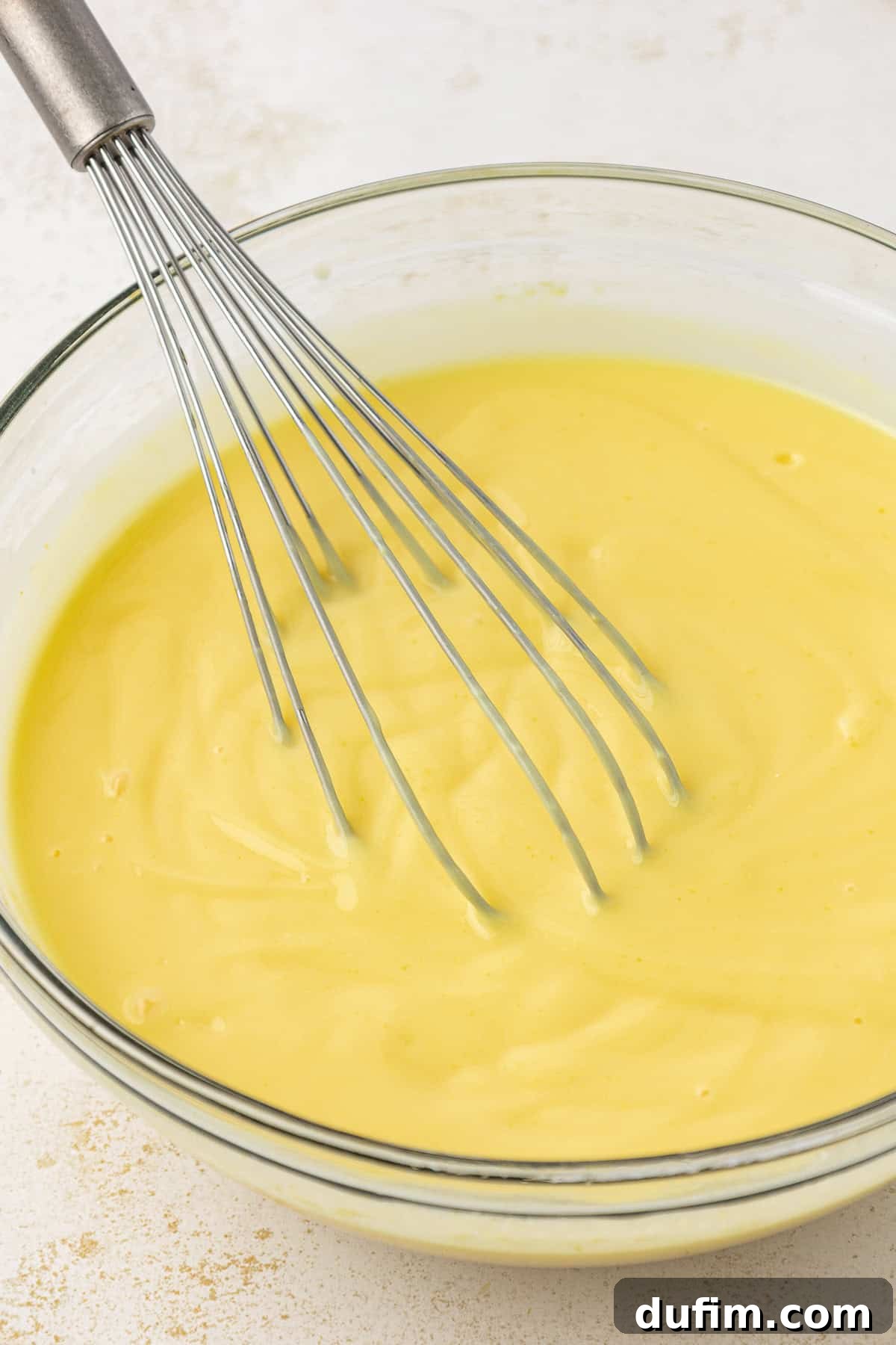 Mastering Delicious Dirt Cake 6 Instant vanilla pudding mixture being whisked in a clear glass bowl, showing its transformation into a thick, creamy consistency.