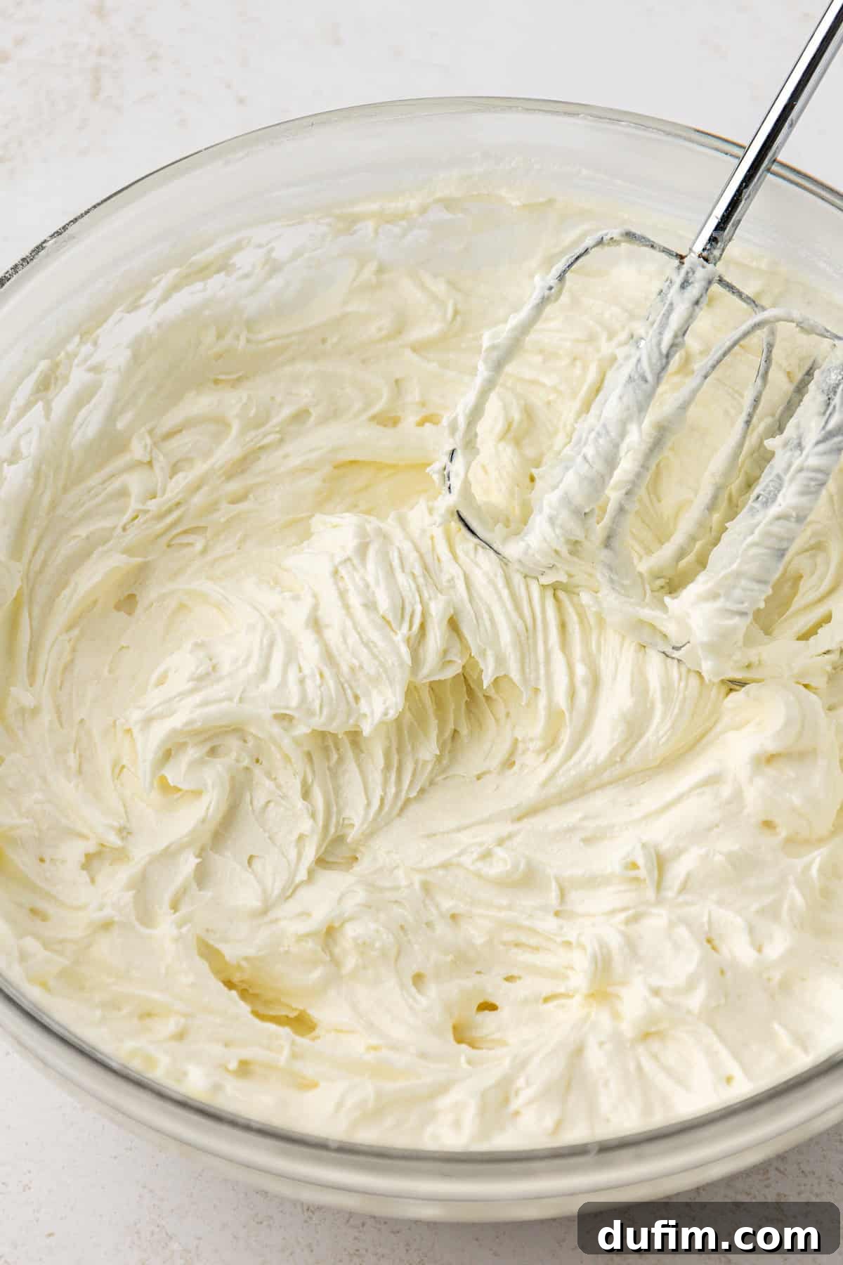 Mastering Delicious Dirt Cake 8 The fully combined cream cheese, butter, and powdered sugar mixture resting in a clear glass bowl after being beaten with an electric mixer, showcasing its smooth and fluffy texture.