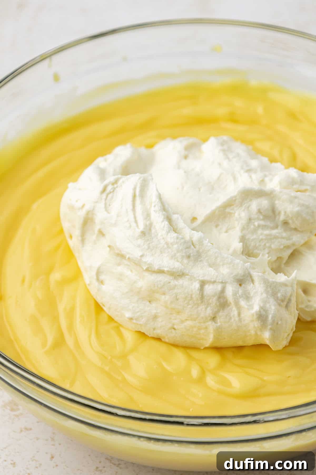 Mastering Delicious Dirt Cake 9 The vibrant vanilla pudding mixture in a large clear glass bowl, with a dollop of the rich cream cheese mixture delicately placed on top, ready to be gently folded together.