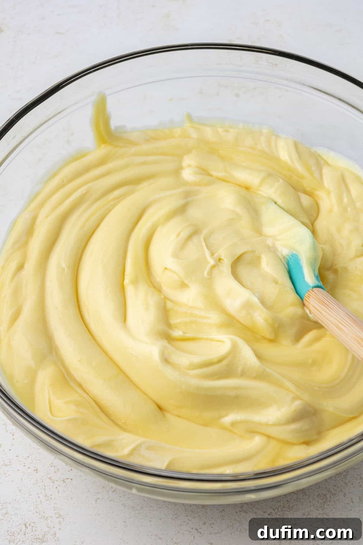 Mastering Delicious Dirt Cake 10 All the creamy pudding layer ingredients expertly combined in a large clear glass bowl, blended into a uniform, smooth, and irresistible filling with a spatula.