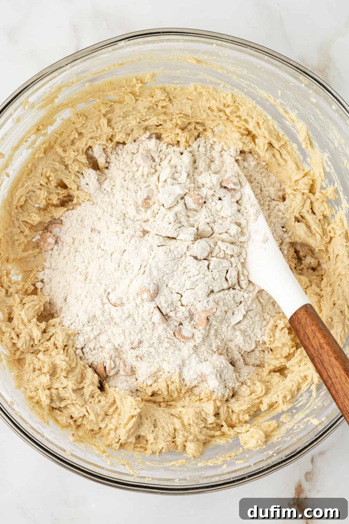 Sweet Butterscotch Chip Delights 11 The combined wet ingredients for butterscotch cookies in a clear glass bowl, with a pile of the pre-mixed dry ingredients waiting to be incorporated on top.
