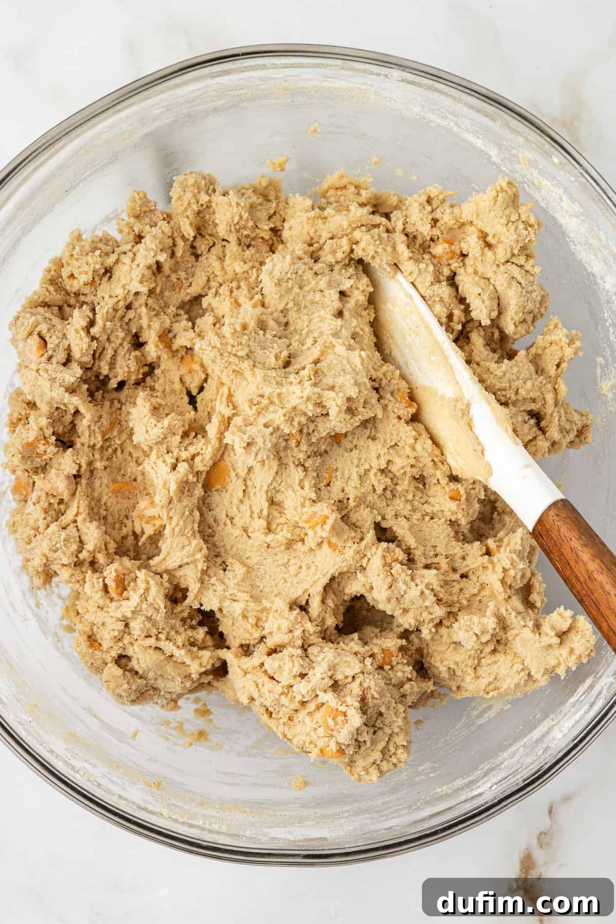 Sweet Butterscotch Chip Delights 12 Finished butterscotch cookie dough resting in a clear glass bowl with a white spatula leaning inside, showing its thick and ready-to-bake consistency.